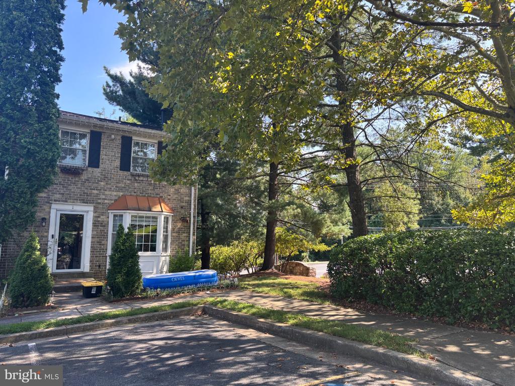 Brick townhouse exterior with a bay window, mature trees, and landscaped parking area.