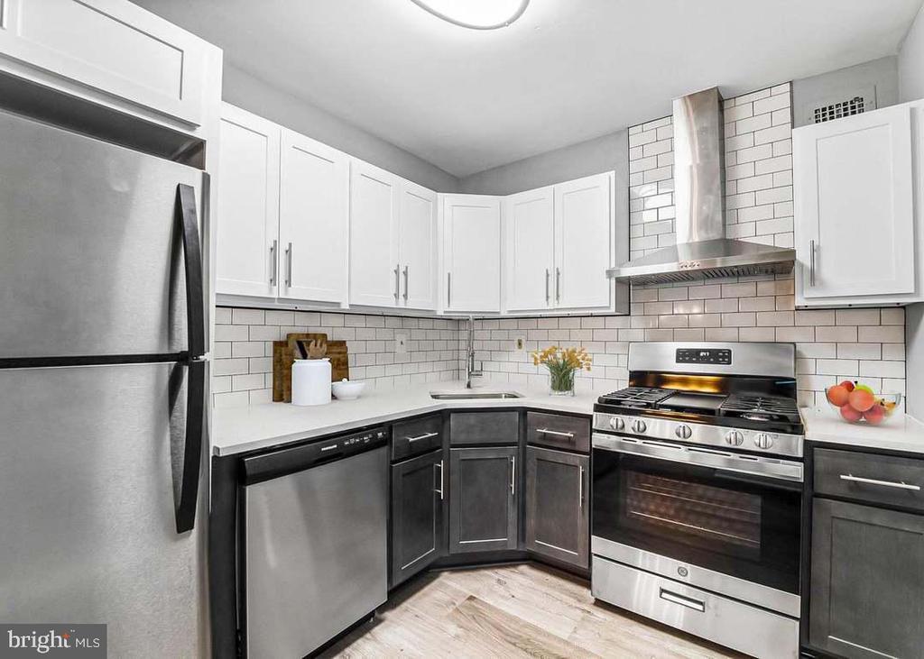 Kitchen with white subway tile, dark lower cabinets, stainless steel appliances, and a corner sink.