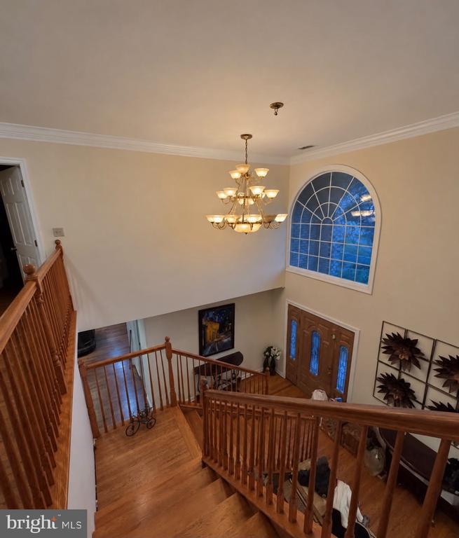 Two-story foyer with a wooden staircase, arched window, chandelier, and double front doors.