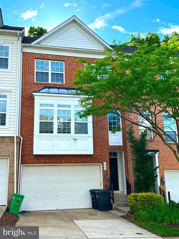 Red-brick townhouse with a white garage door and leafy tree in front.