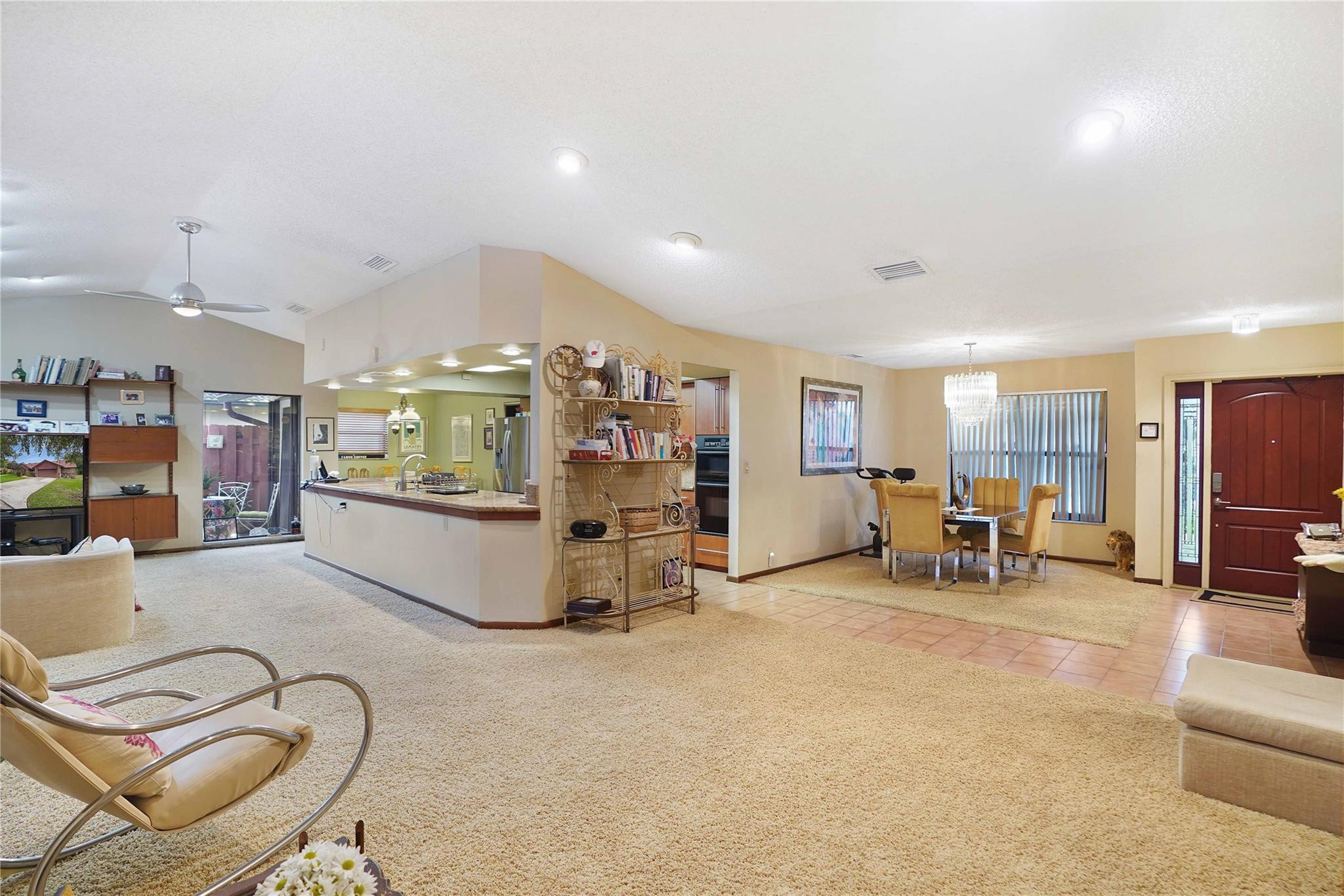 Open-plan living room, kitchen, and dining area with a breakfast counter and beige carpet.