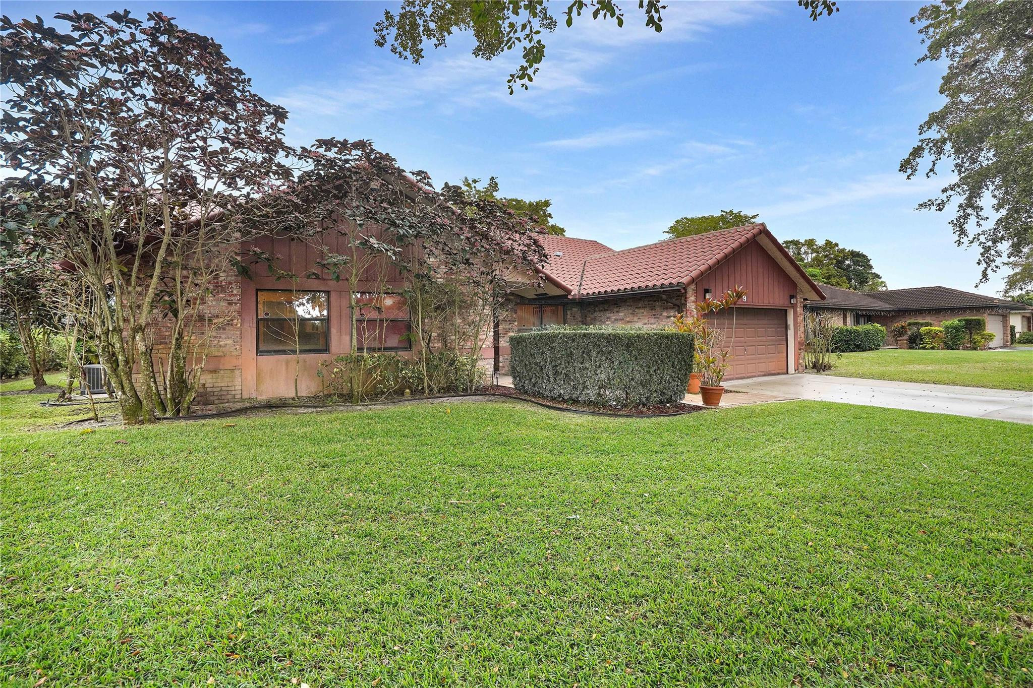Single-story brick-and-wood home with a red tile roof, attached garage, and broad green lawn.