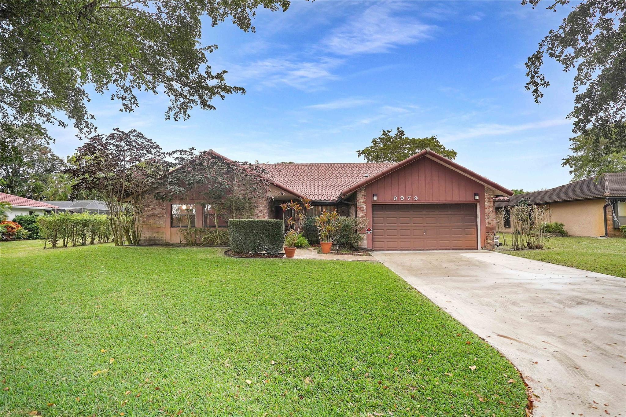 Single-story brick home with a reddish tile roof, attached garage, and broad front lawn.