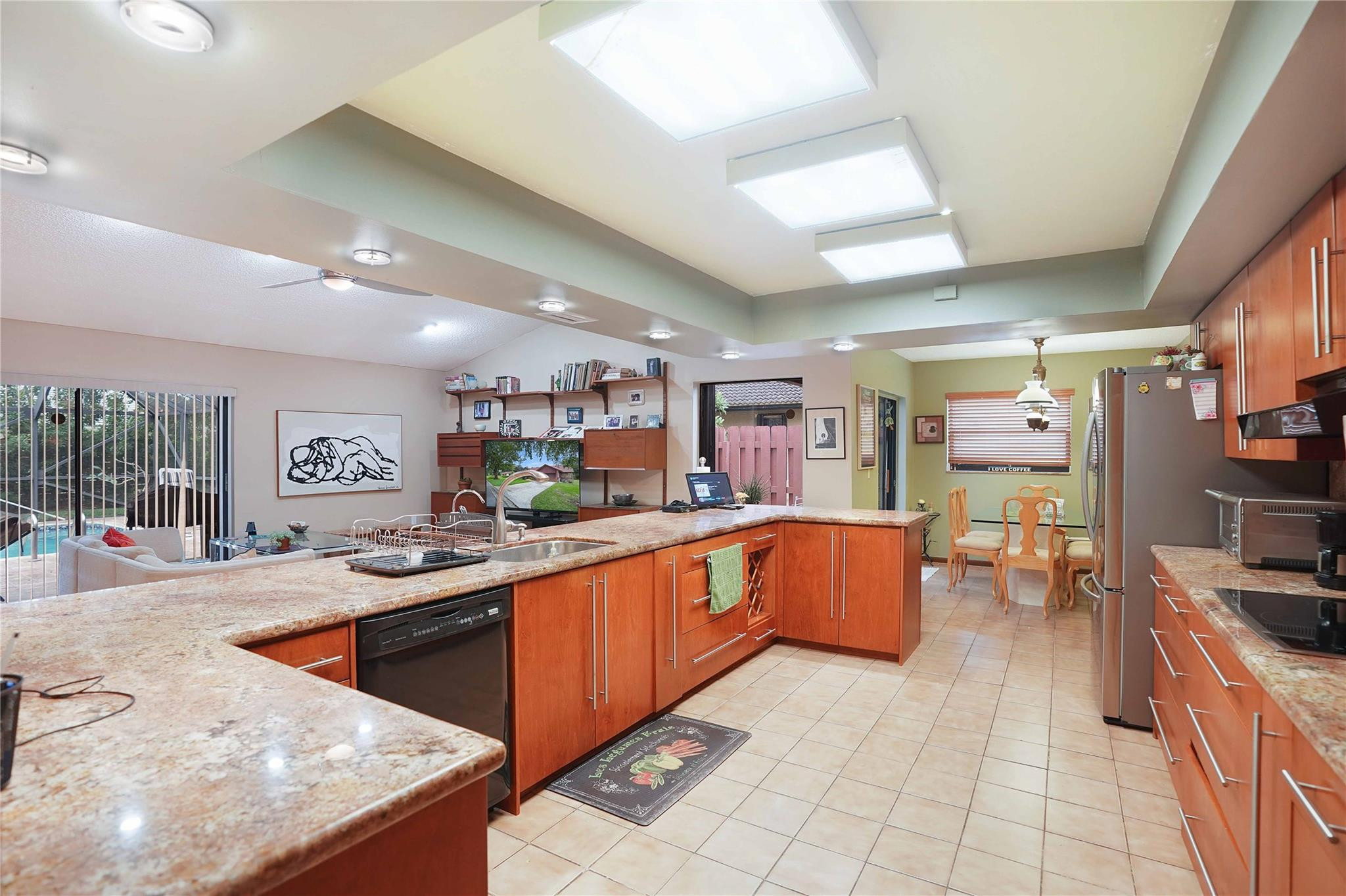 Open-plan kitchen with reddish wood cabinetry, granite island, and dining area beside sliding doors to a pool.