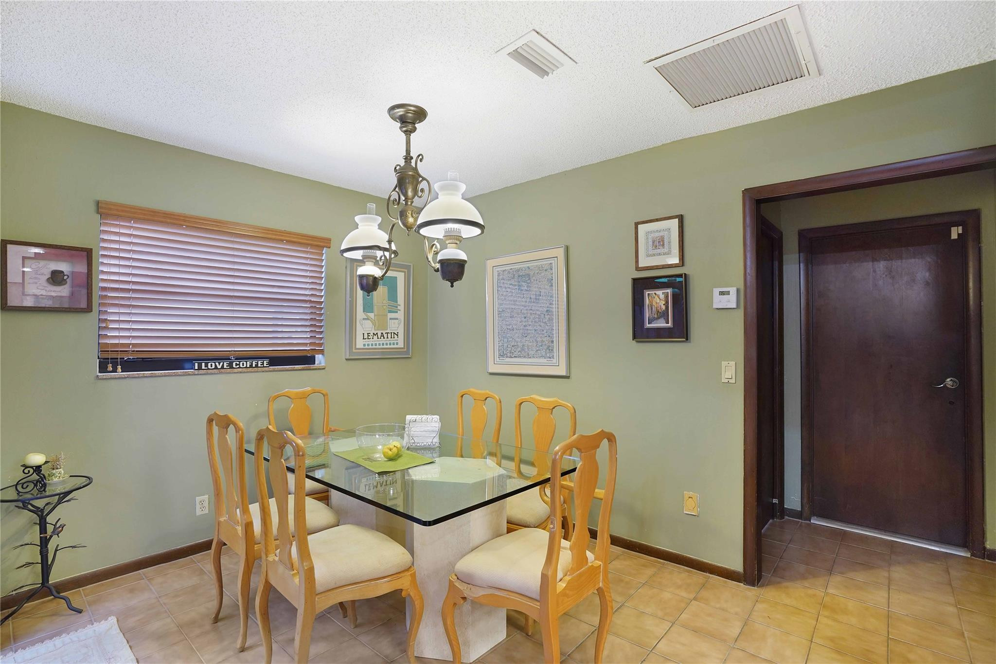 Dining room with a glass-top table, light wood chairs, and a decorative chandelier.