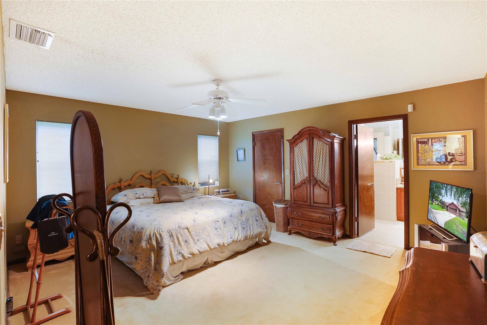 Bedroom with a floral-covered bed, ornate wooden armoire, and open doorway to the bathroom.