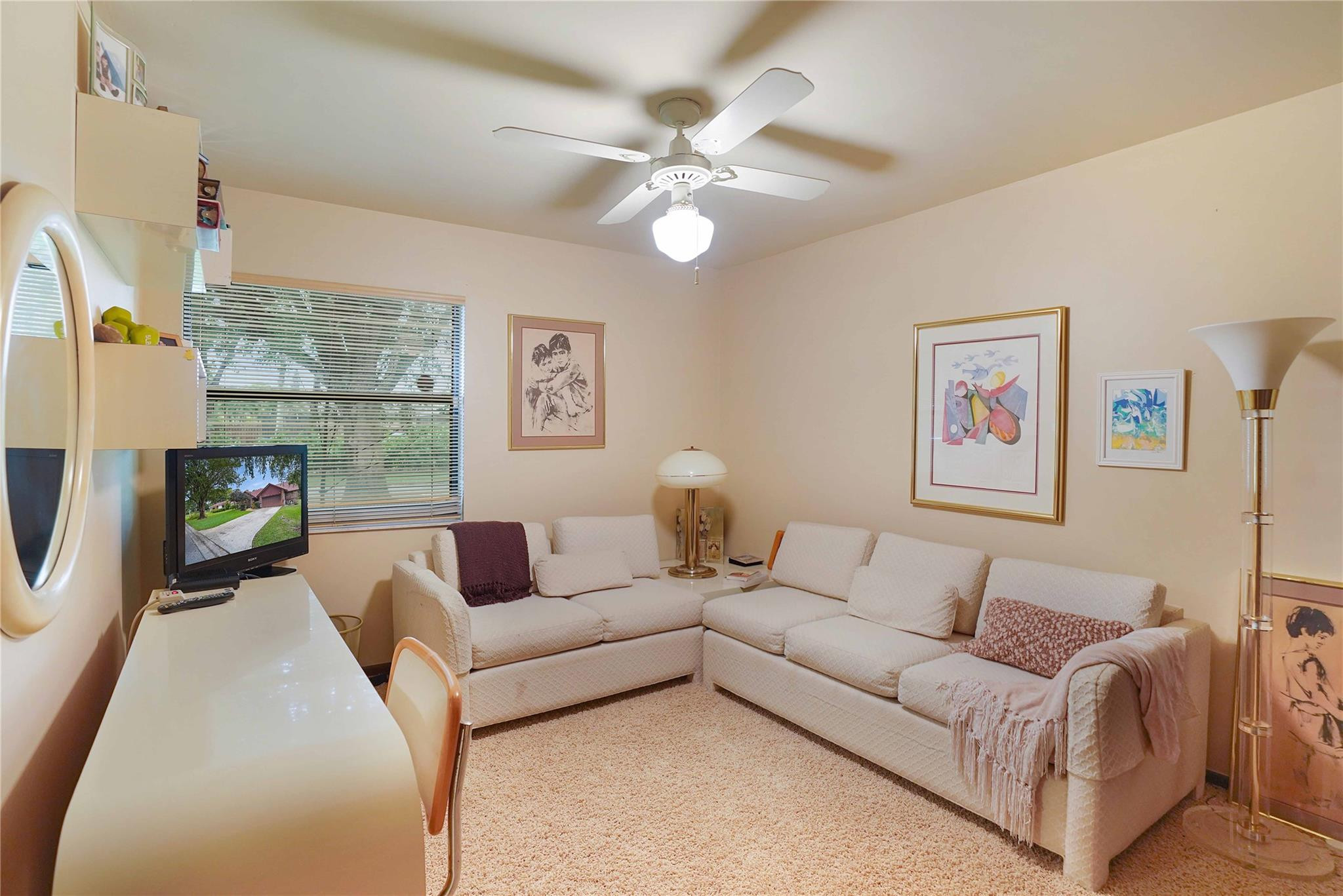 Living room with cream sofas, framed artwork, a television, and a window with blinds.