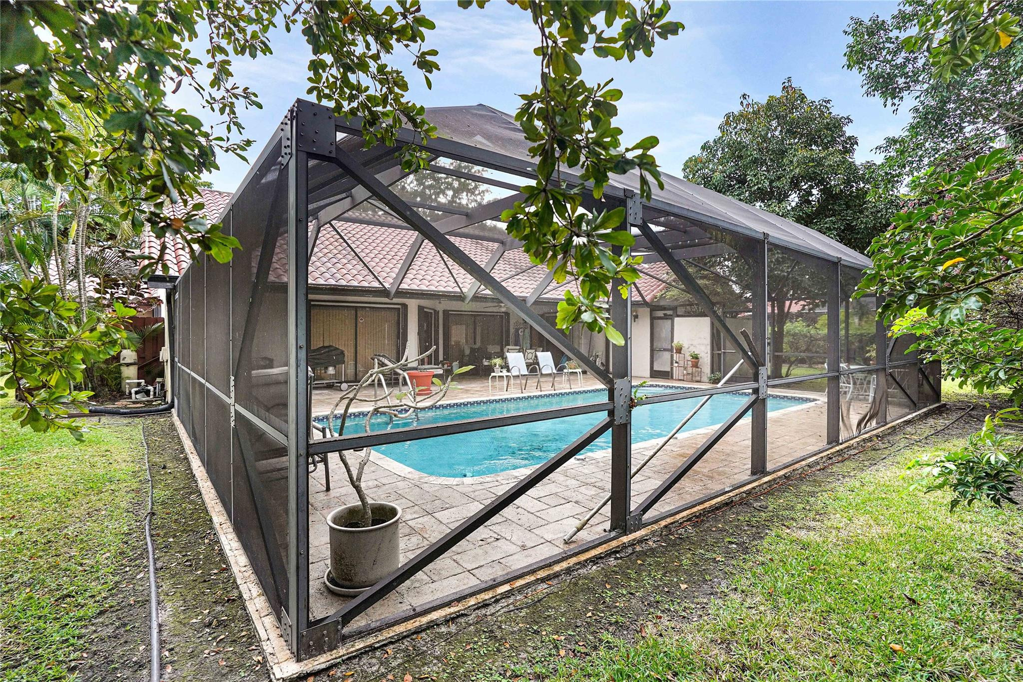 Screened backyard pool with a paved deck and patio seating, surrounded by tropical greenery.