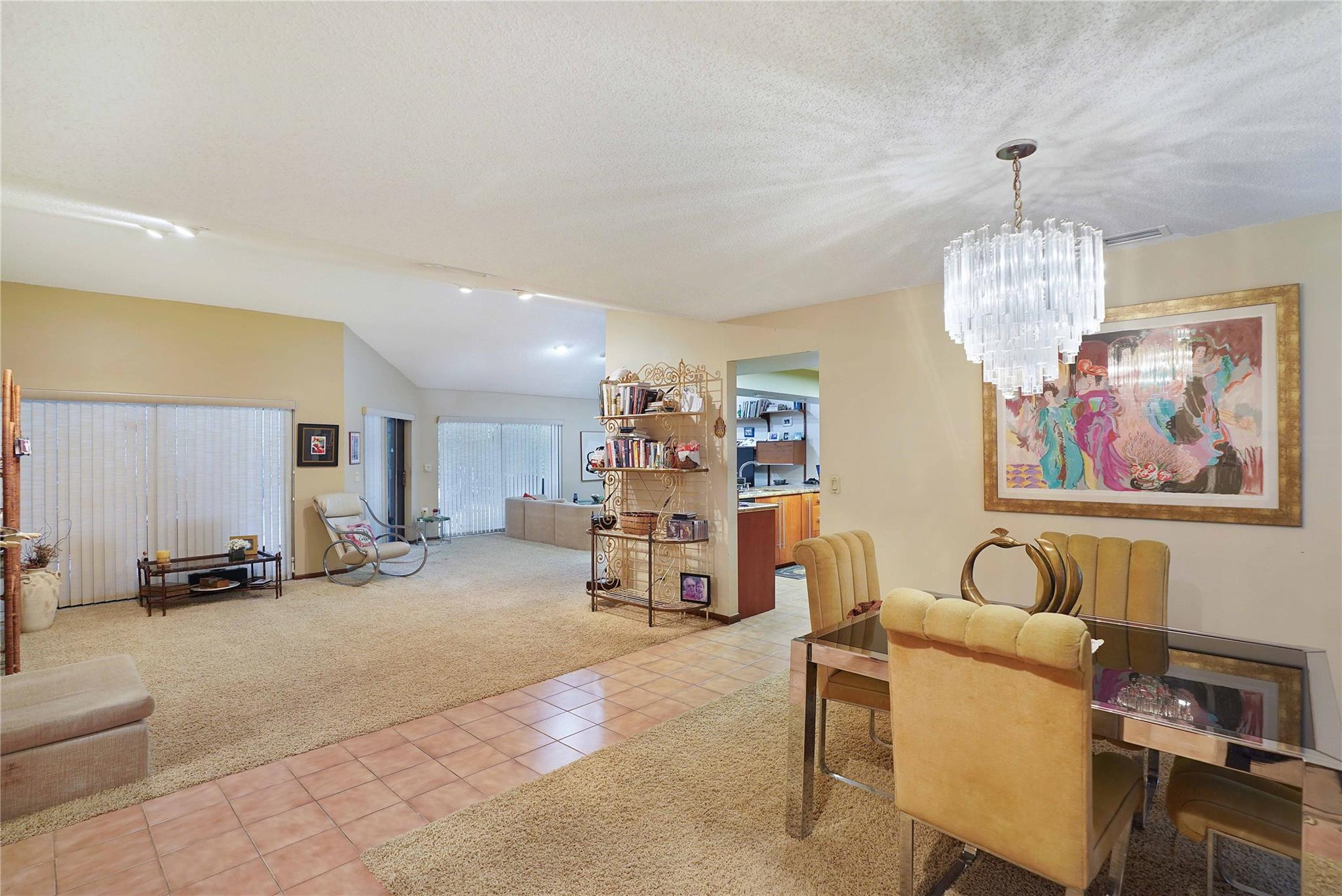 Open-plan living and dining room with yellow chairs, a glass-top table, and a striking chandelier.