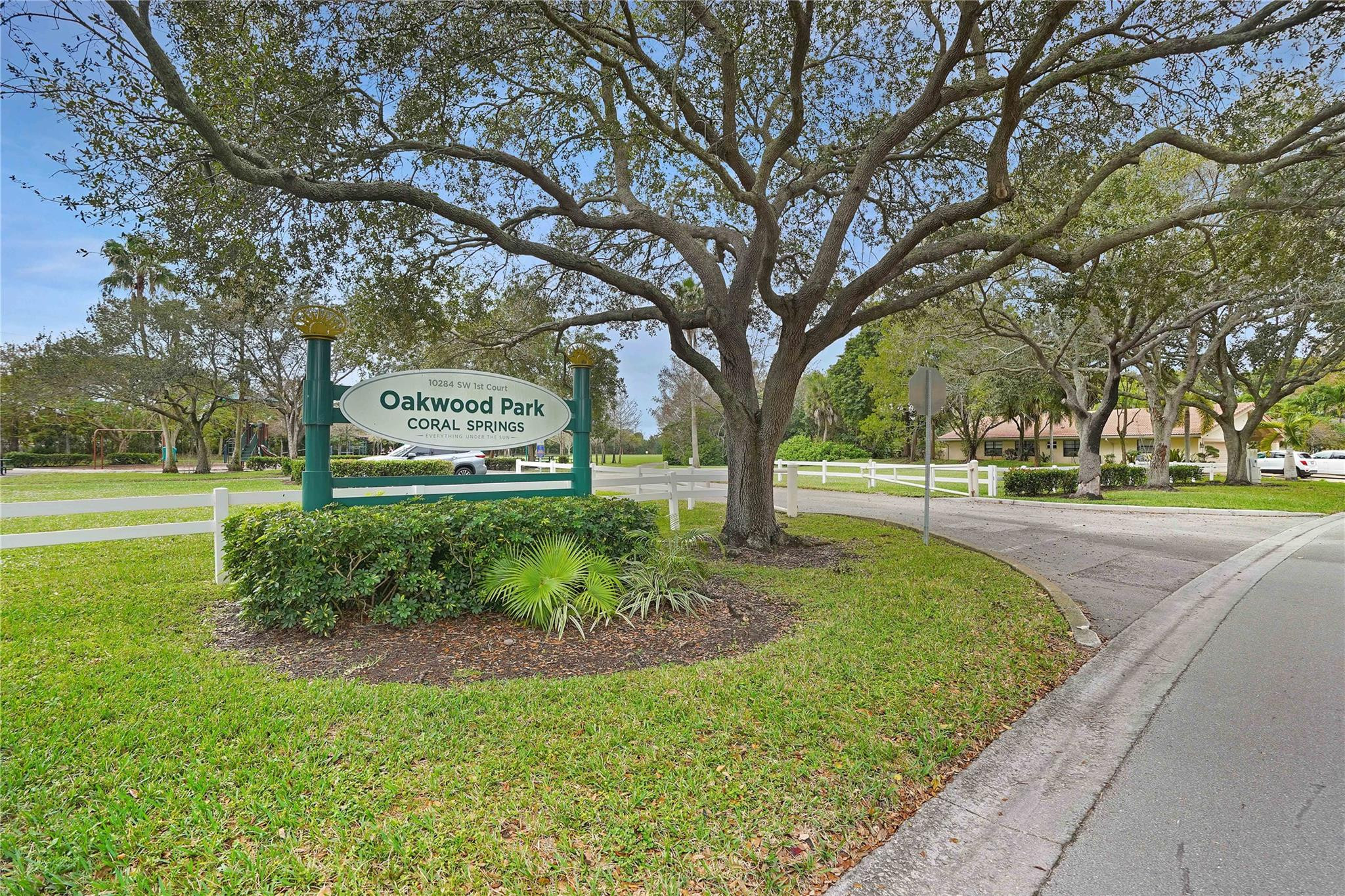 Oakwood Park entrance sign beneath a large tree, with white fencing and landscaped grounds.