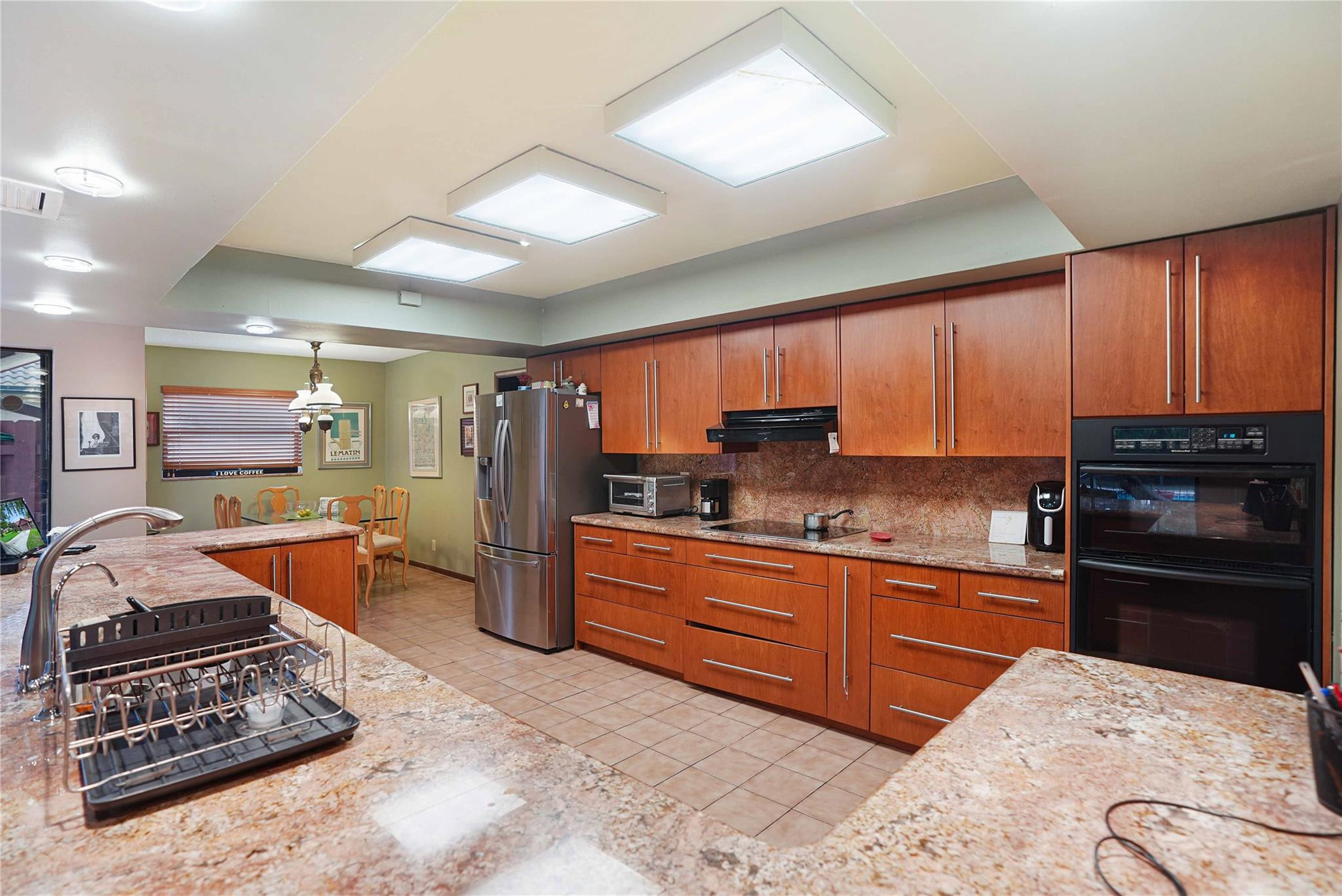 Kitchen with reddish wood cabinetry, granite counters, stainless steel appliances, and a large sink island.