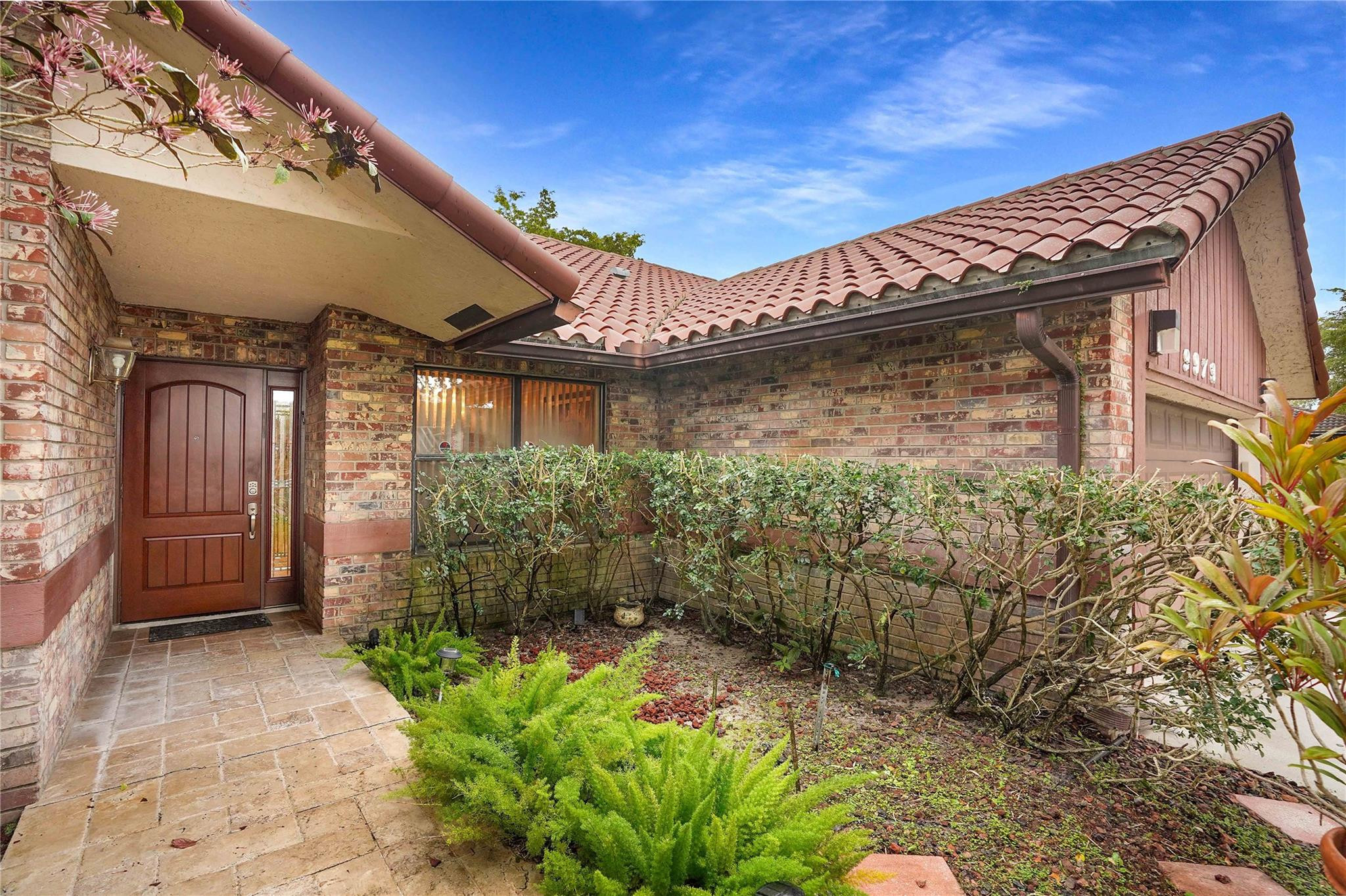 Brick home entrance with a red tile roof, brown door, and landscaped walkway.