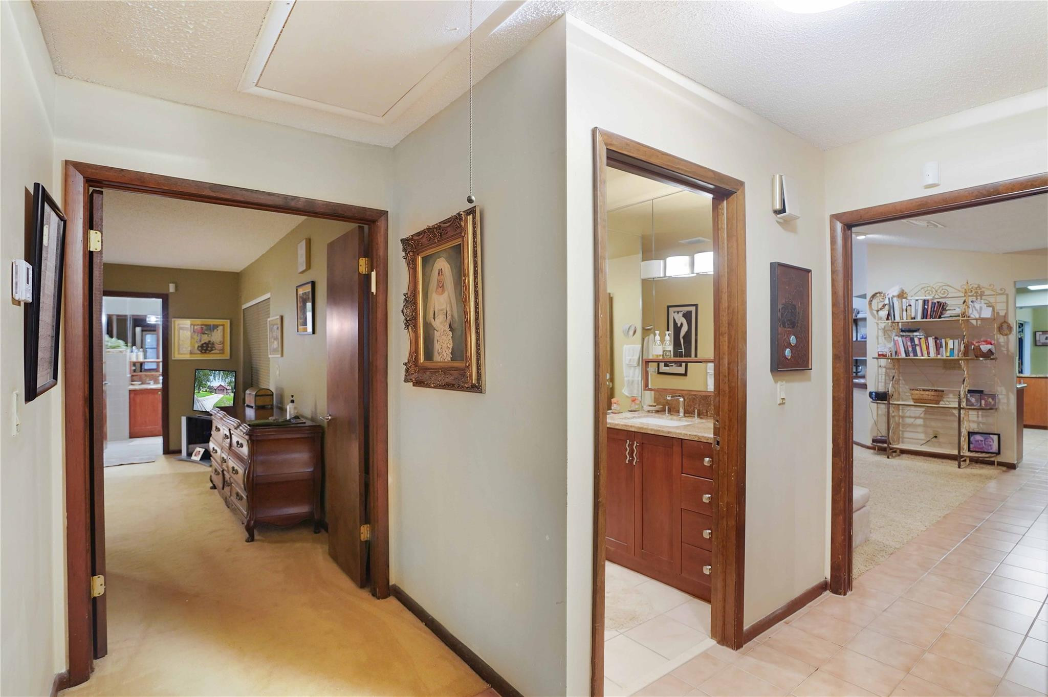 Tiled hallway with dark wood trim and open doorways to a bathroom and furnished rooms.