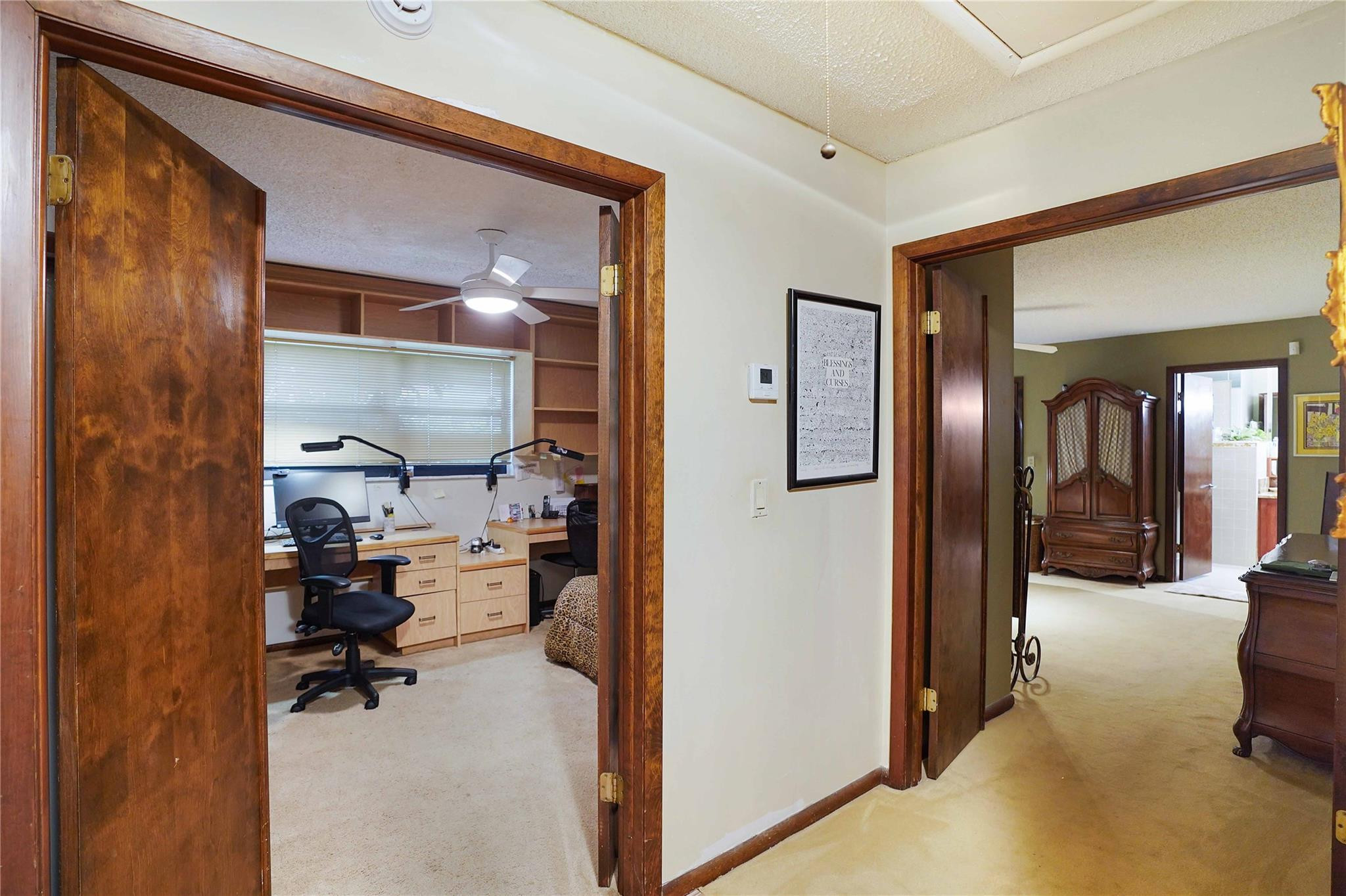 Hallway between a home office and bedroom, with dark wood doorframes and built-in office shelving.