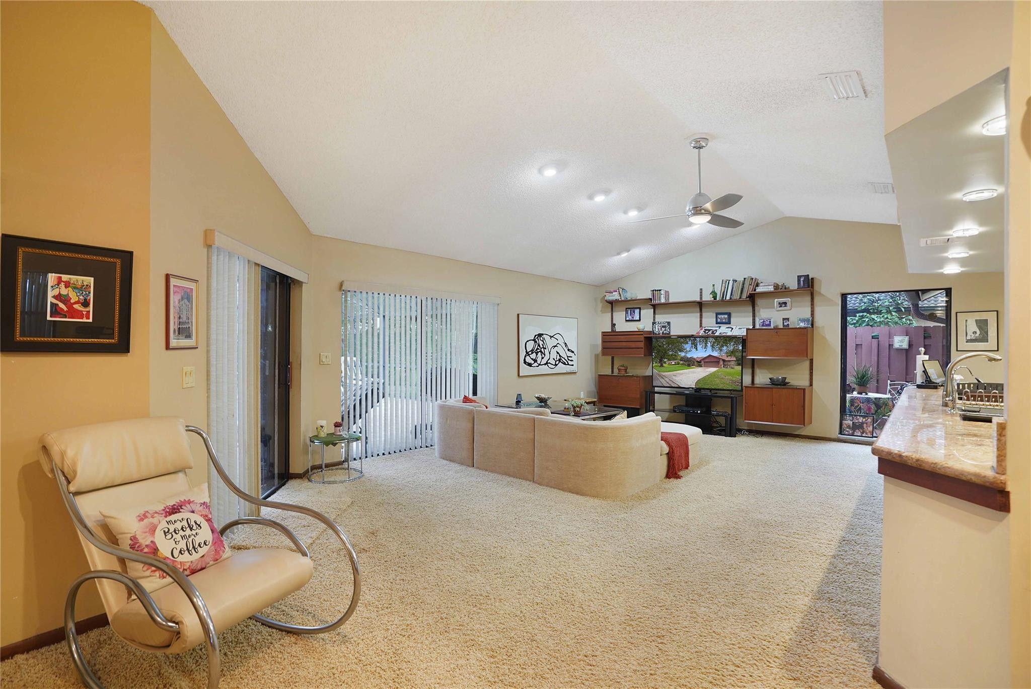 Furnished living room with vaulted ceiling, built-in shelving, and sliding glass doors.