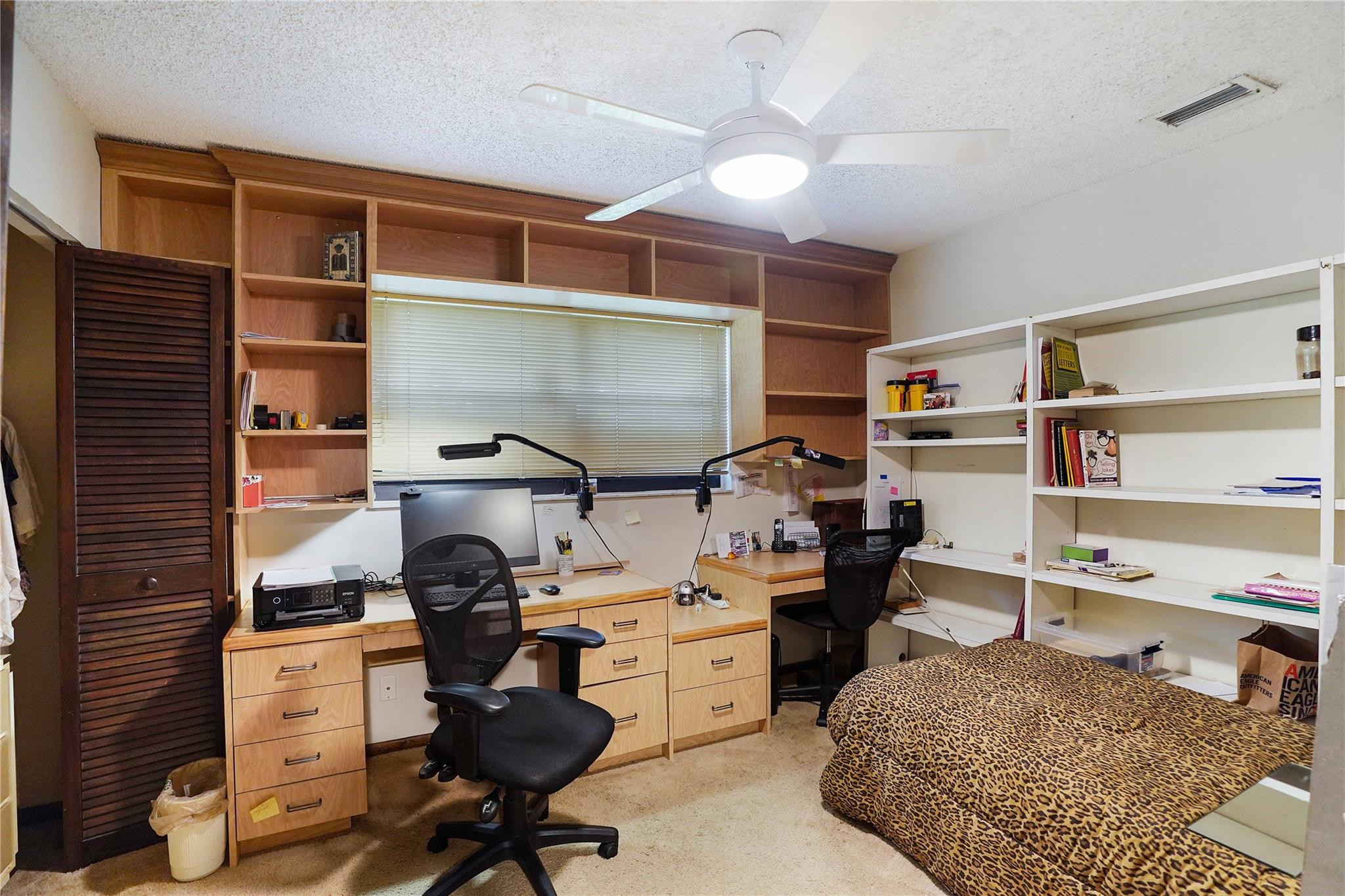 Bedroom office with built-in wood desks, extensive shelving, and a leopard-print bedspread.