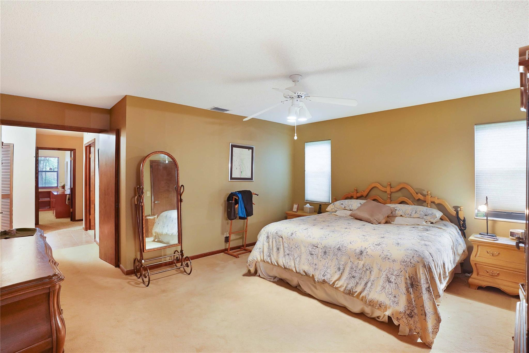 Furnished bedroom with a large floral bed, carved wooden headboard, and arched full-length mirror.