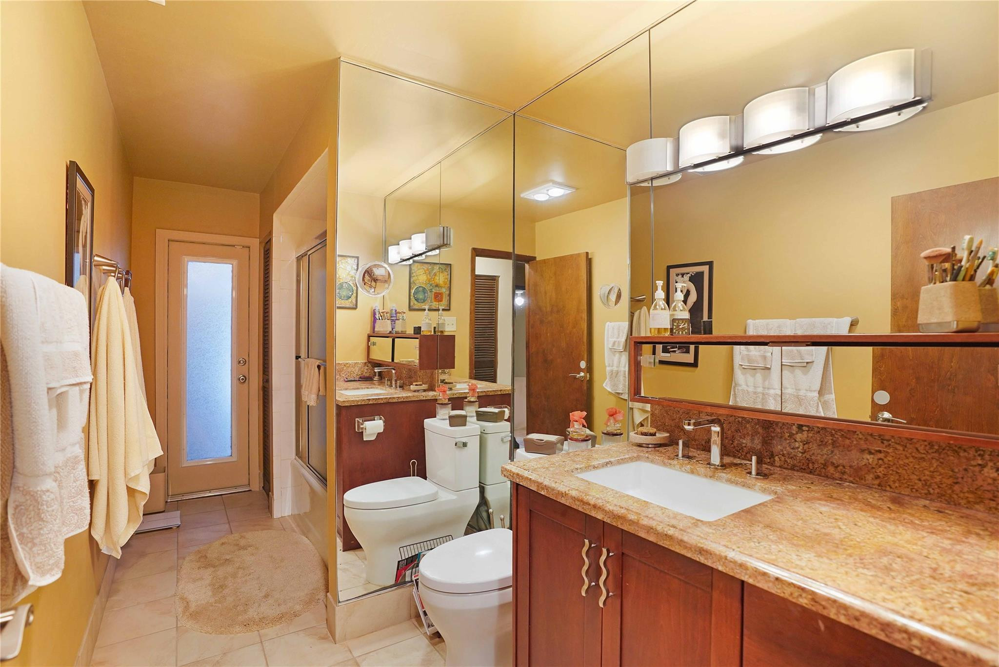 Bathroom with a long granite-topped vanity, mirrored wall, and glass-enclosed shower.