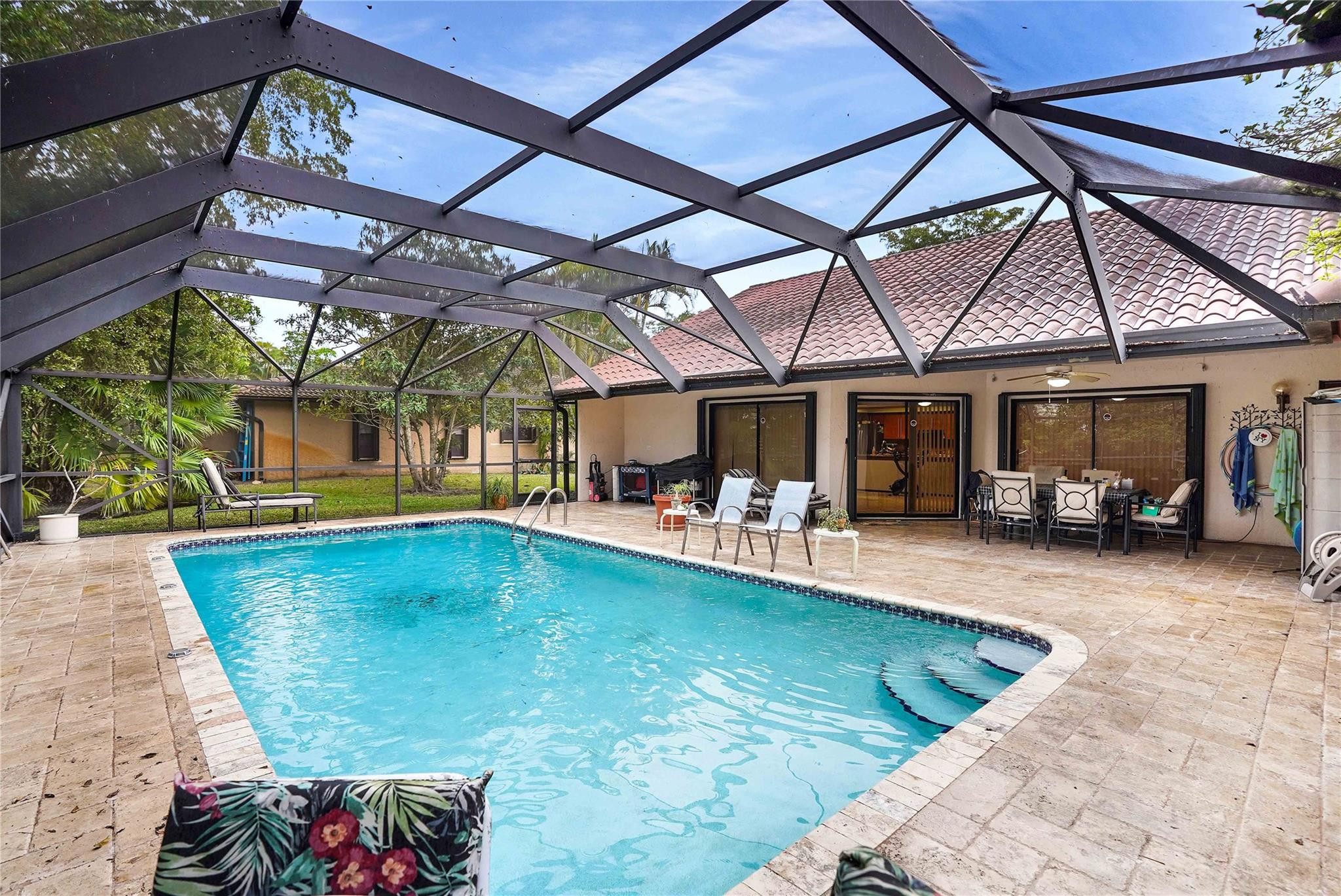 Backyard swimming pool beneath a screened enclosure, with a tiled patio and outdoor seating.