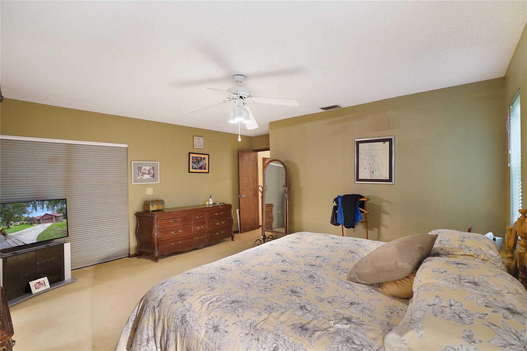 Furnished bedroom with floral bedding, a wooden dresser, and a white ceiling fan.