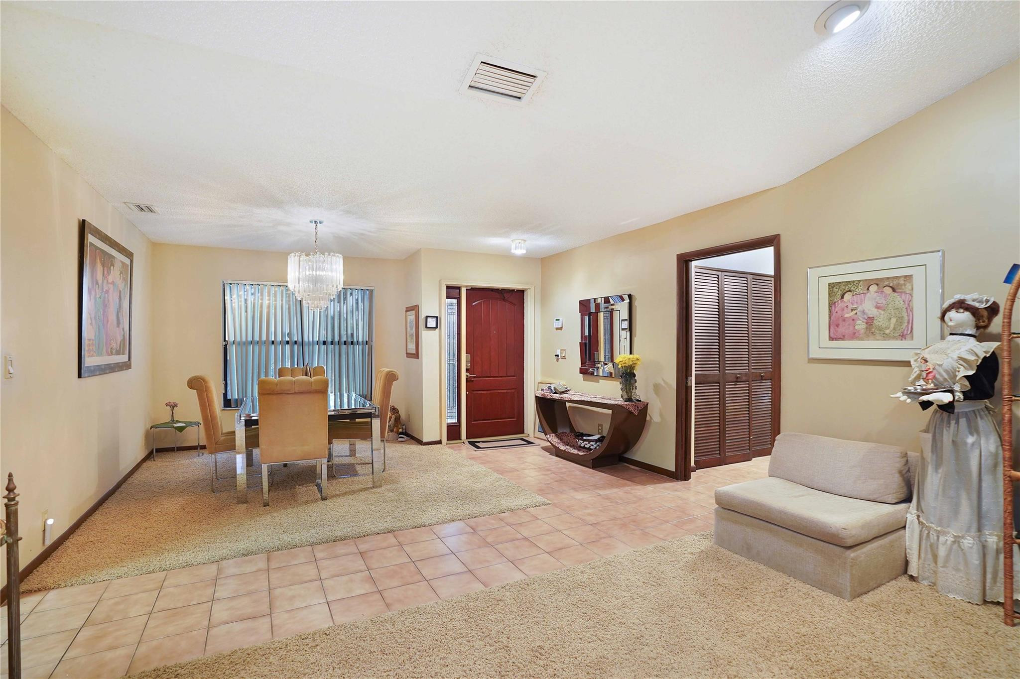 Entry and dining area with a red front door, chandelier, and tiled walkway.