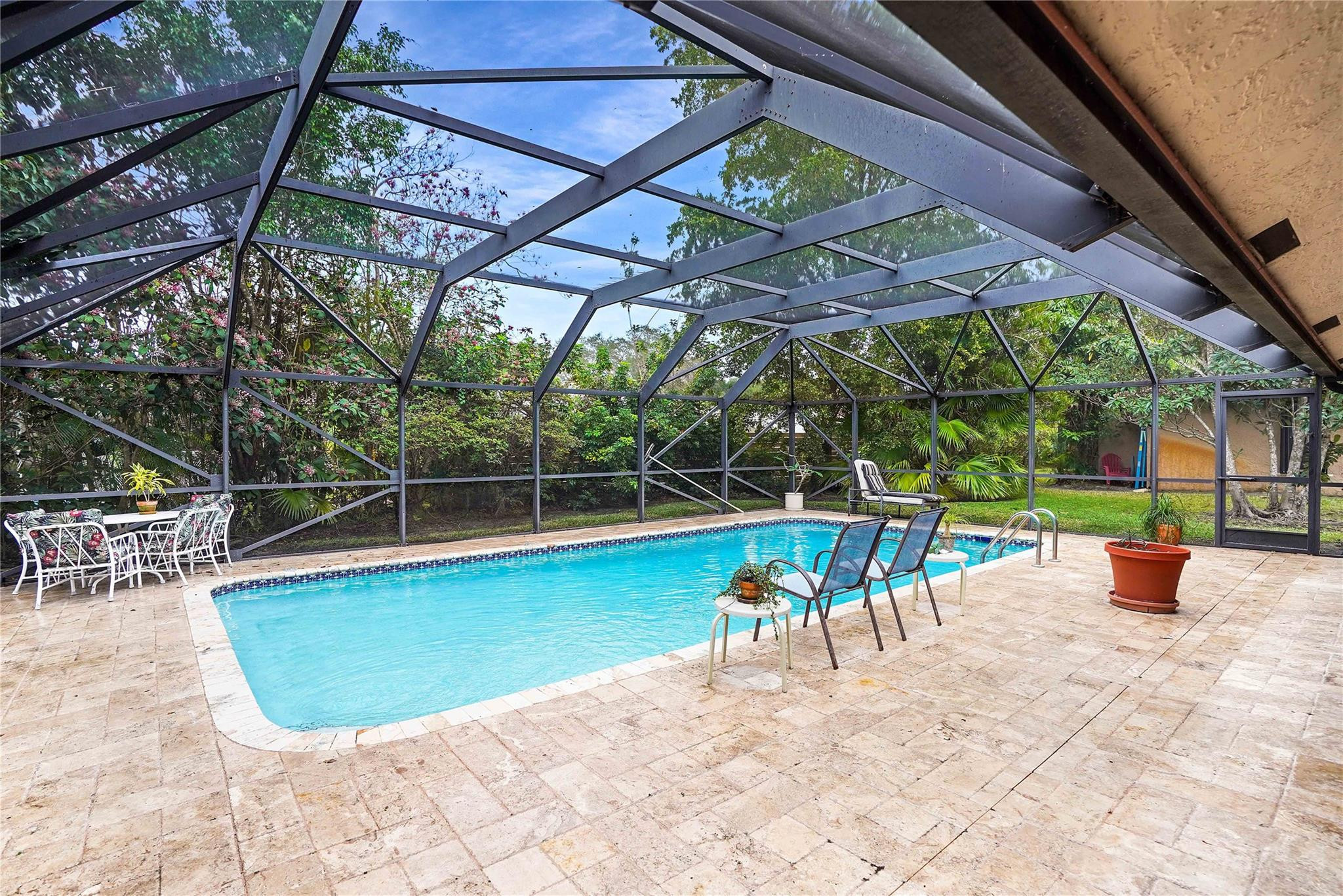 Swimming pool in a screened enclosure with stone patio and lounge chairs