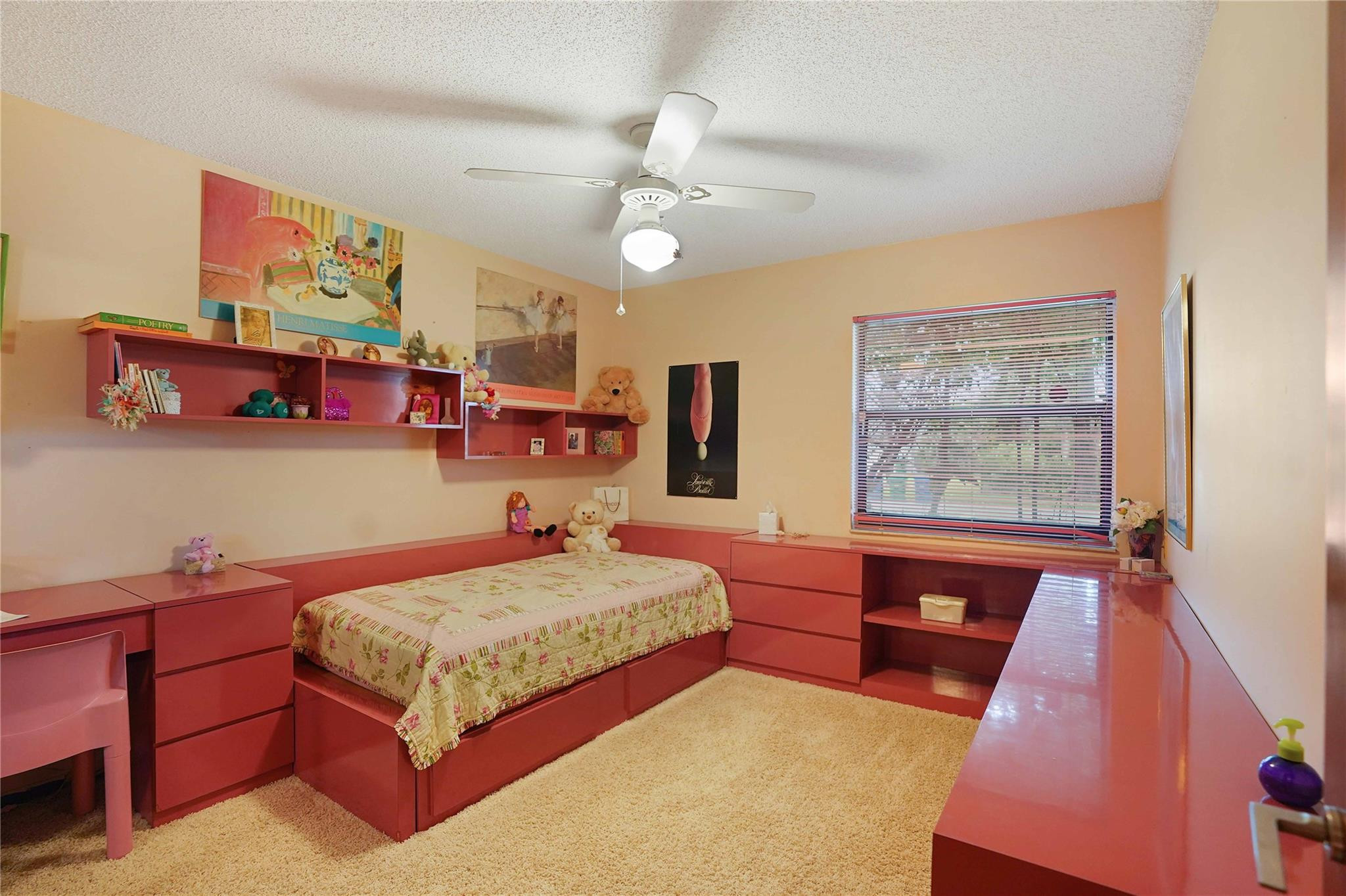 Bedroom with a built-in red bed and desk, wall shelves, stuffed animals, and a floral quilt.