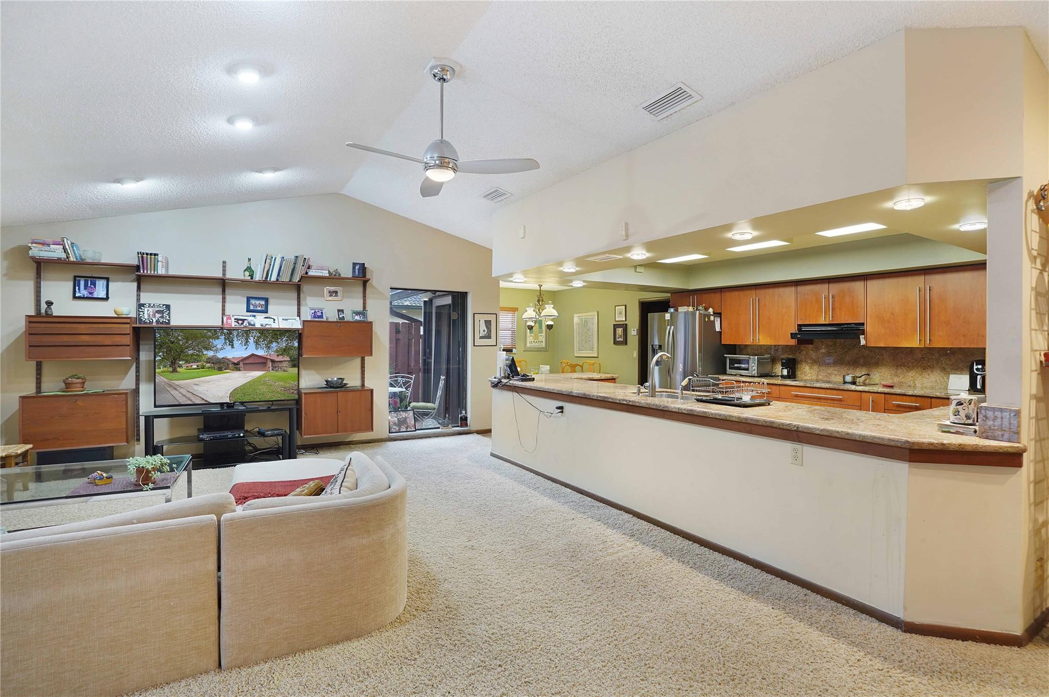 Open-plan living room and kitchen with a curved sofa, wood cabinetry, and a long breakfast bar.