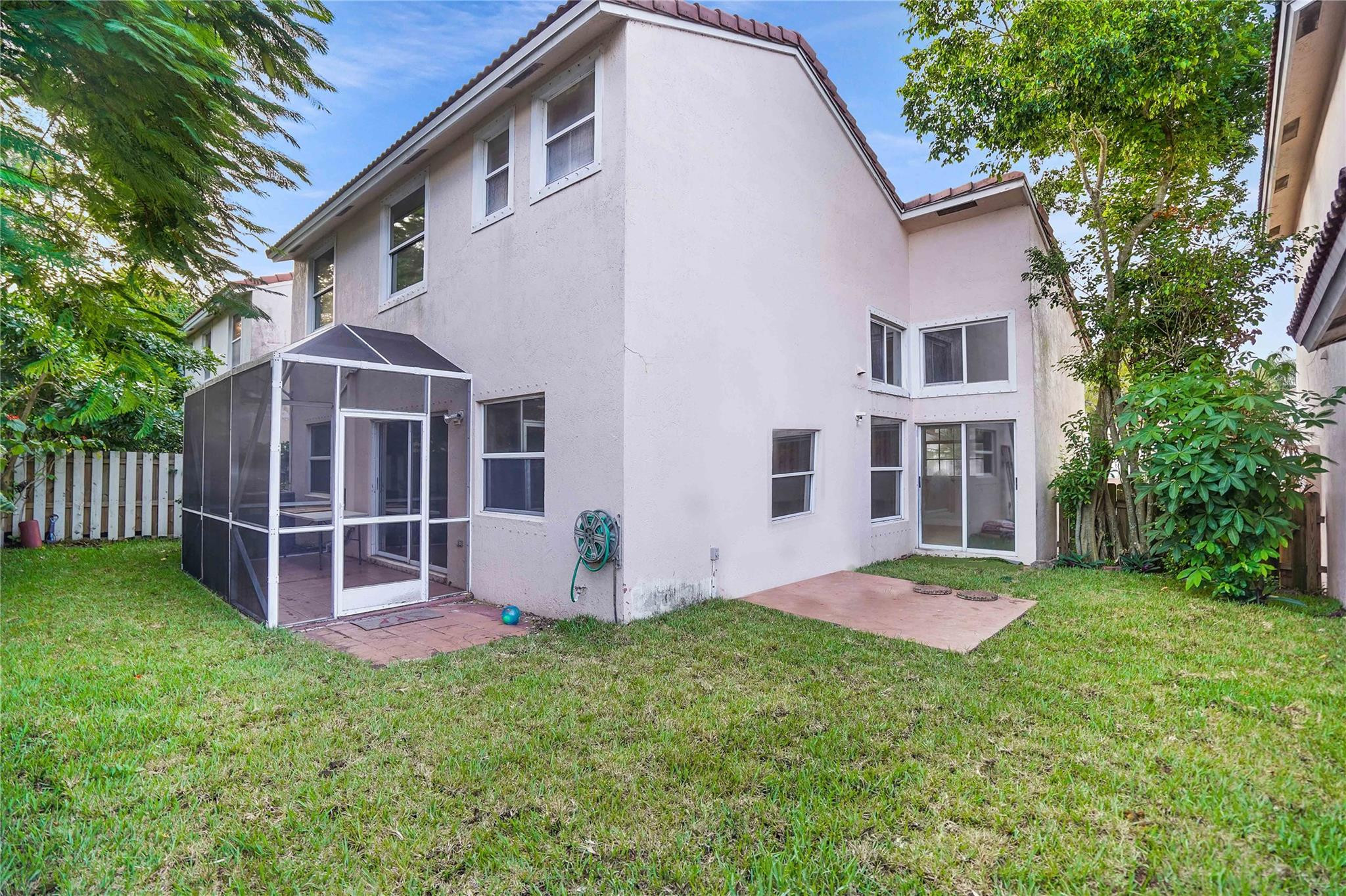Two-story stucco home viewed from the backyard, with a screened patio enclosure and grassy lawn.