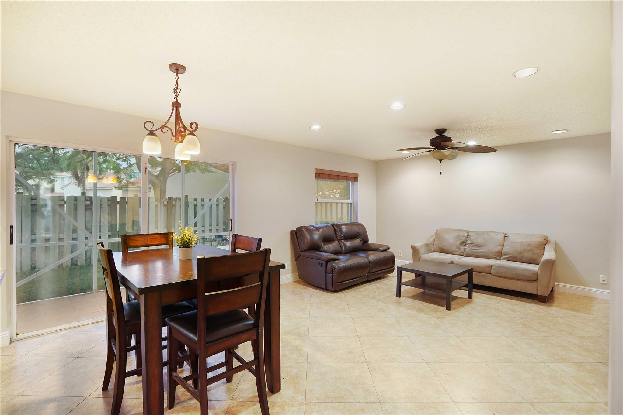 Open-plan living and dining room with tiled floors, a dark wood dining set, and sliding glass doors.