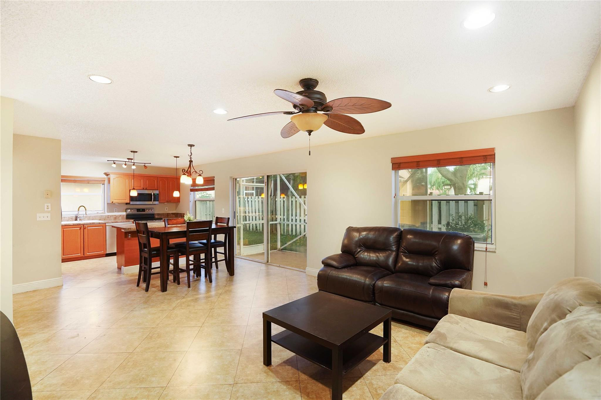 Open-plan living room with dark leather sofa, tiled floors, and sliding doors to a fenced yard.