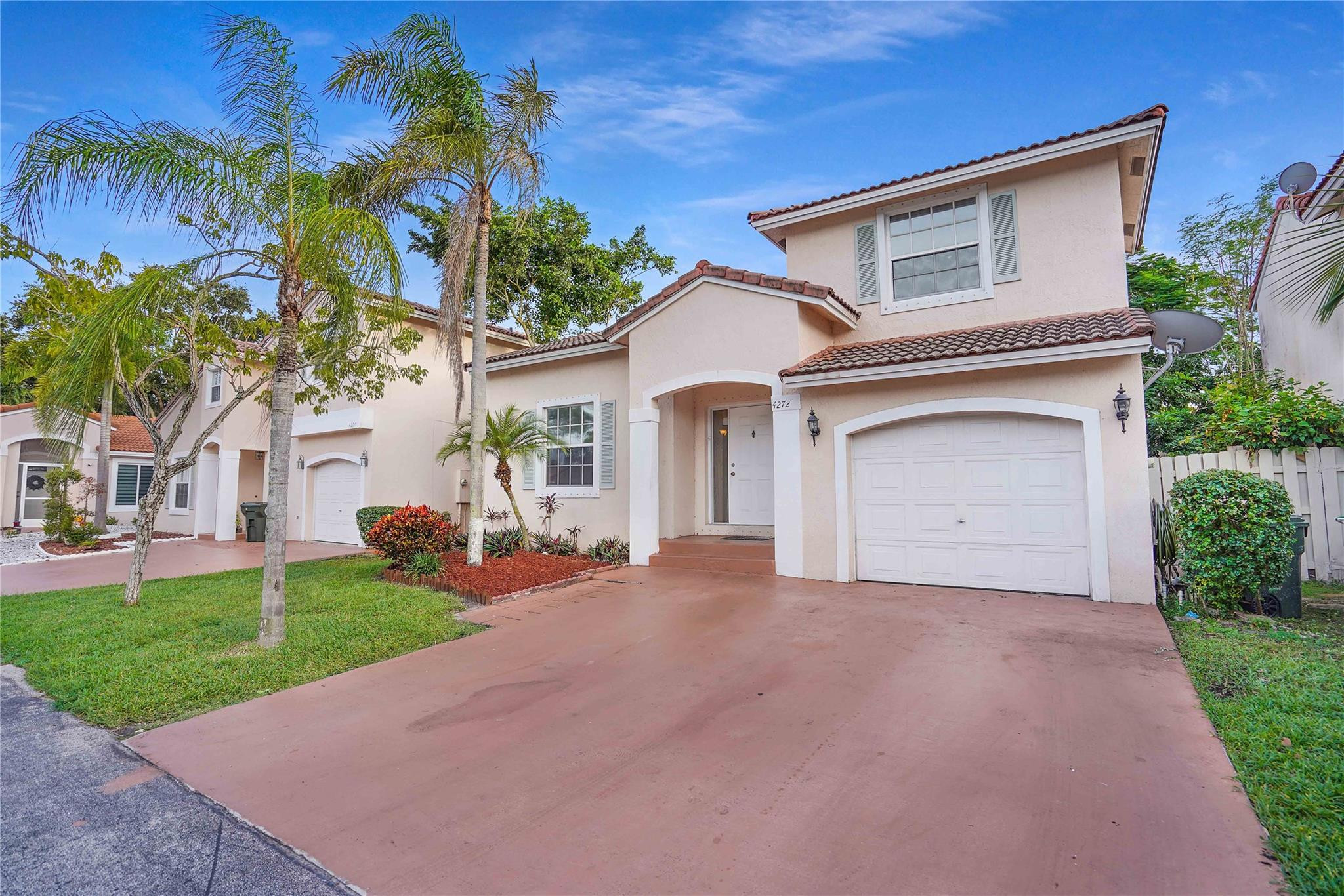 Two-story stucco home with a red tile roof, palm trees, and a wide driveway.