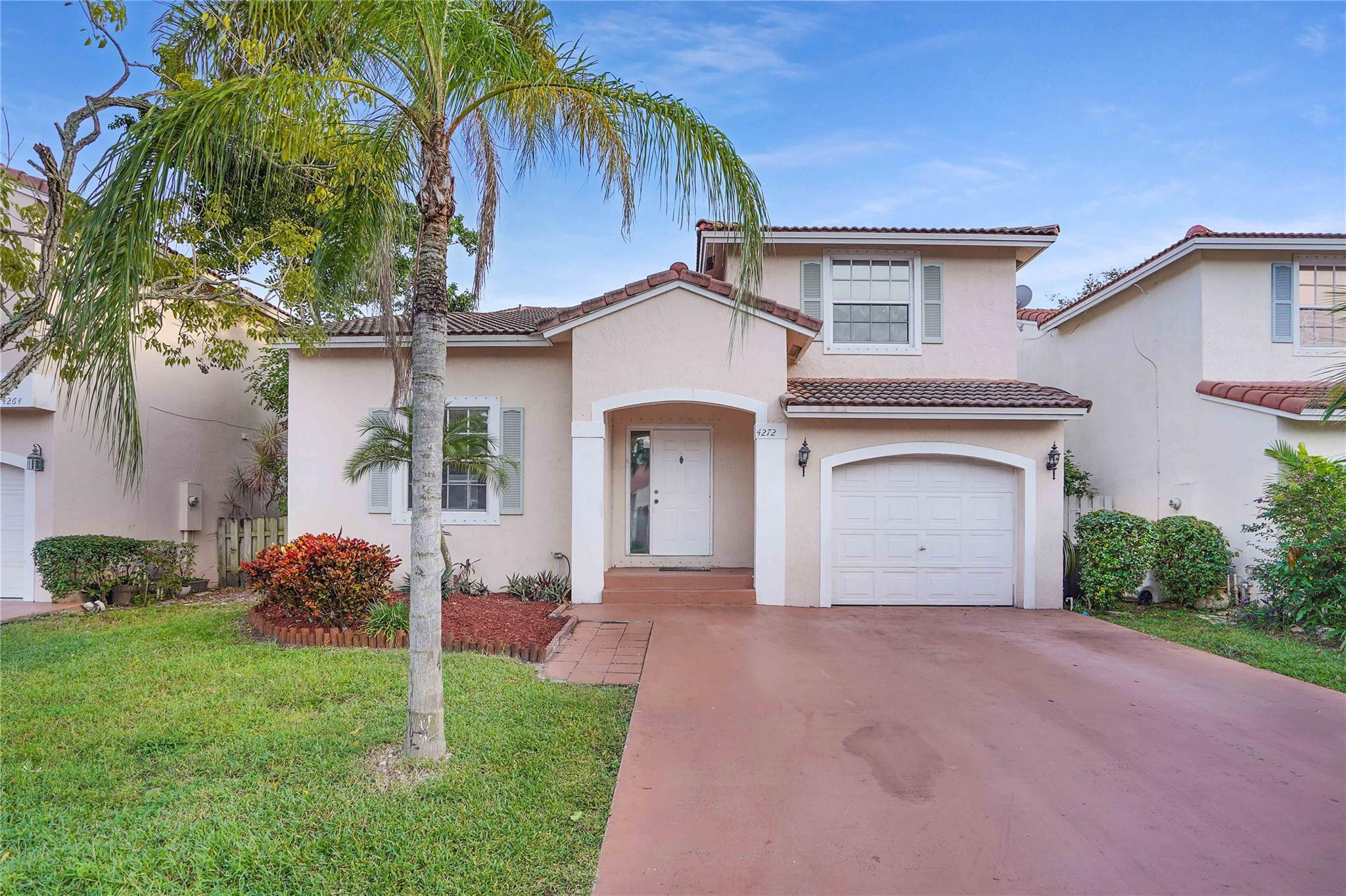 Two-story stucco home with a red tile roof, arched entry, garage, and palm tree in front.