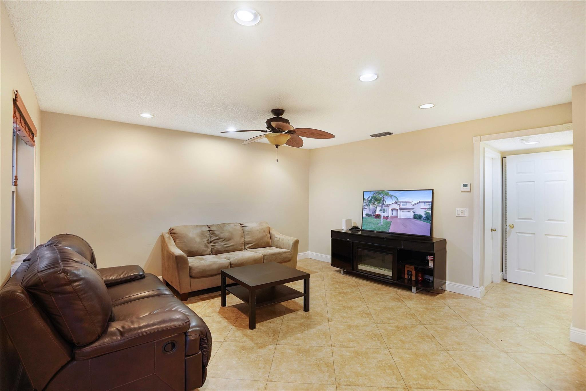 Furnished living room with leather seating, tiled floor, ceiling fan, and television.