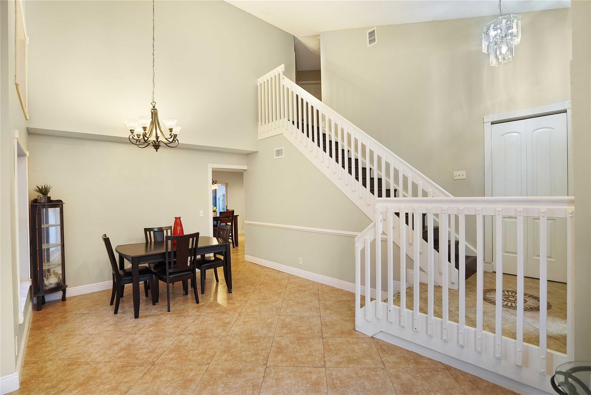 Two-story foyer with a white staircase, tile floors, and a dining table beneath a chandelier.