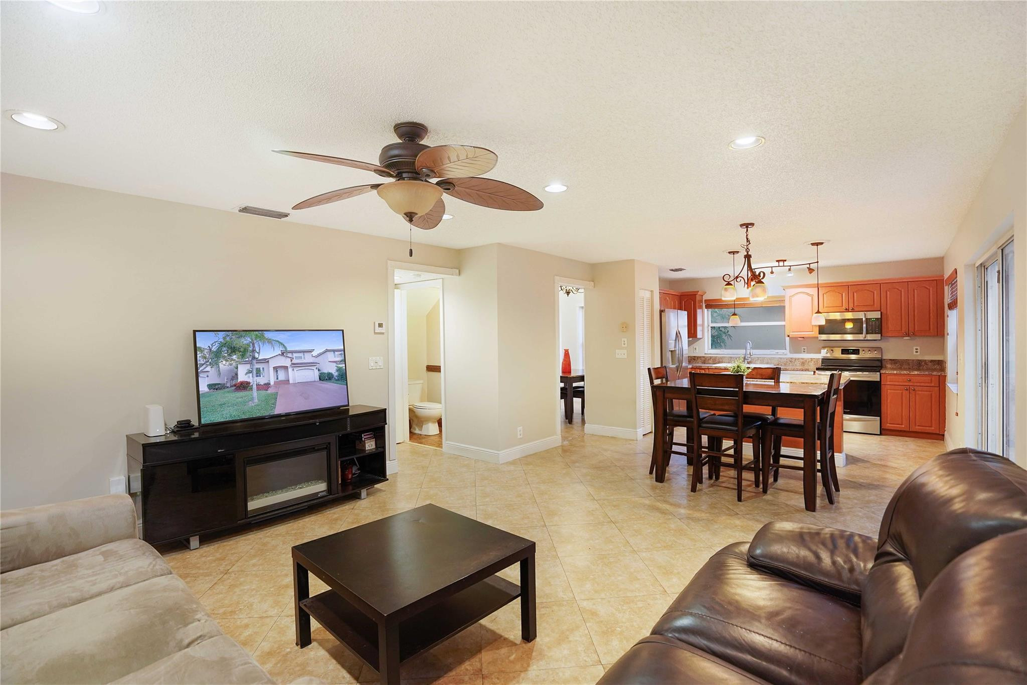 Open-plan living room and kitchen with a ceiling fan, tiled floors, and reddish wood cabinets.
