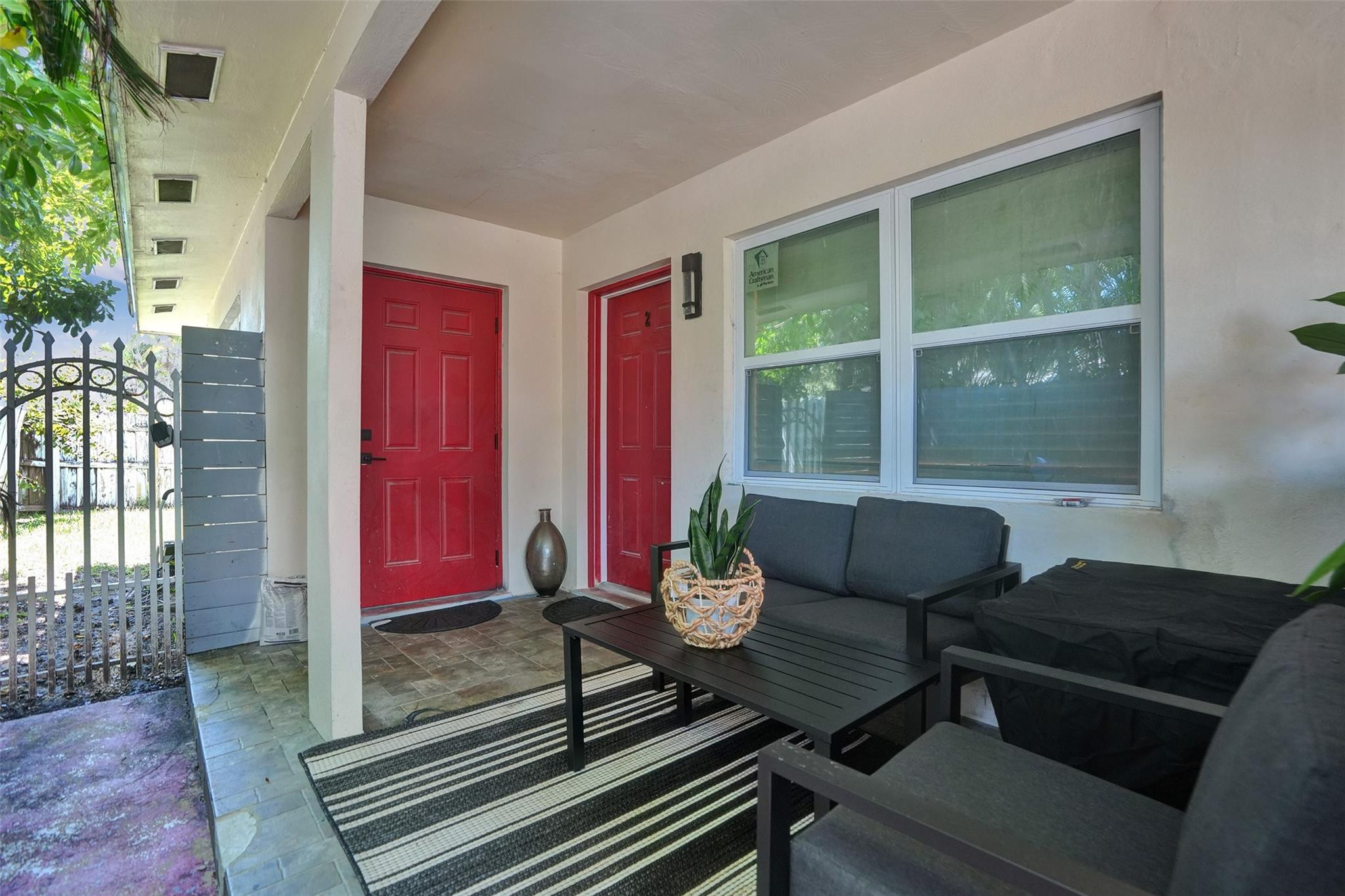 Covered front porch with red doors, black seating, striped rug, and potted plants.