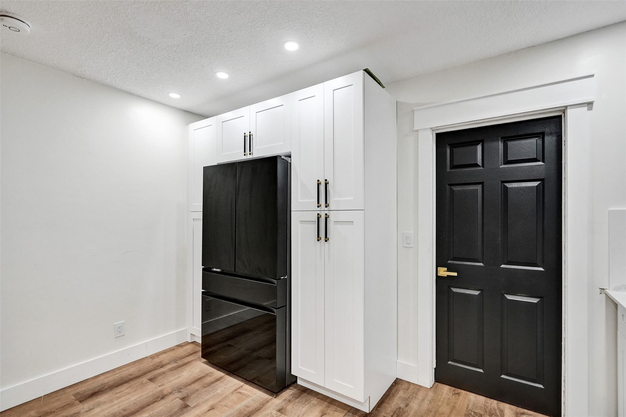 Kitchen with black refrigerator, white built-in cabinets, and a black paneled door.