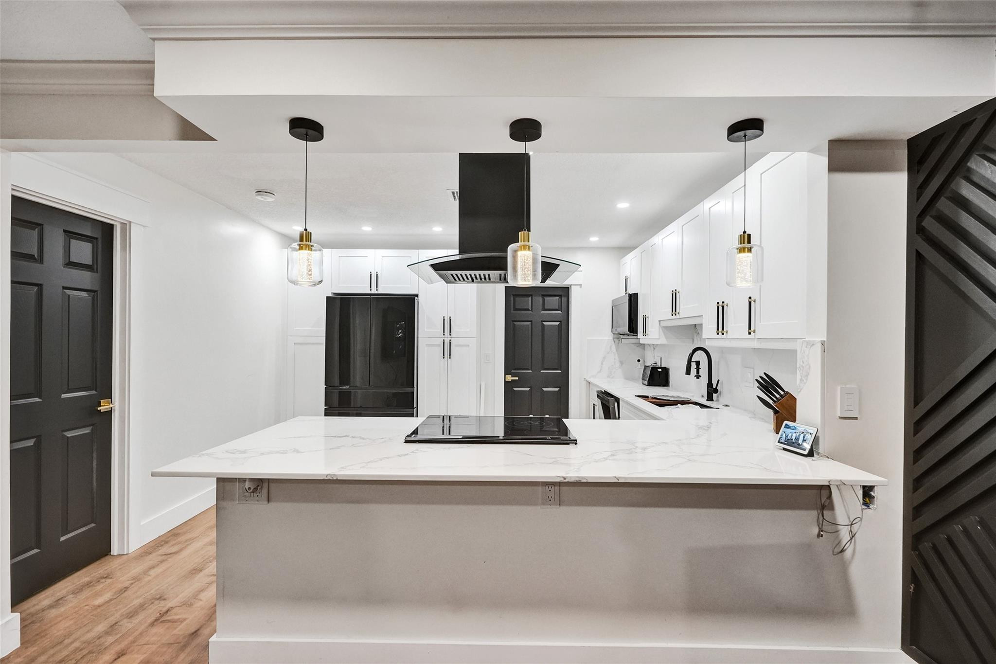 Modern kitchen with a large veined-stone island, induction cooktop, and white cabinetry.