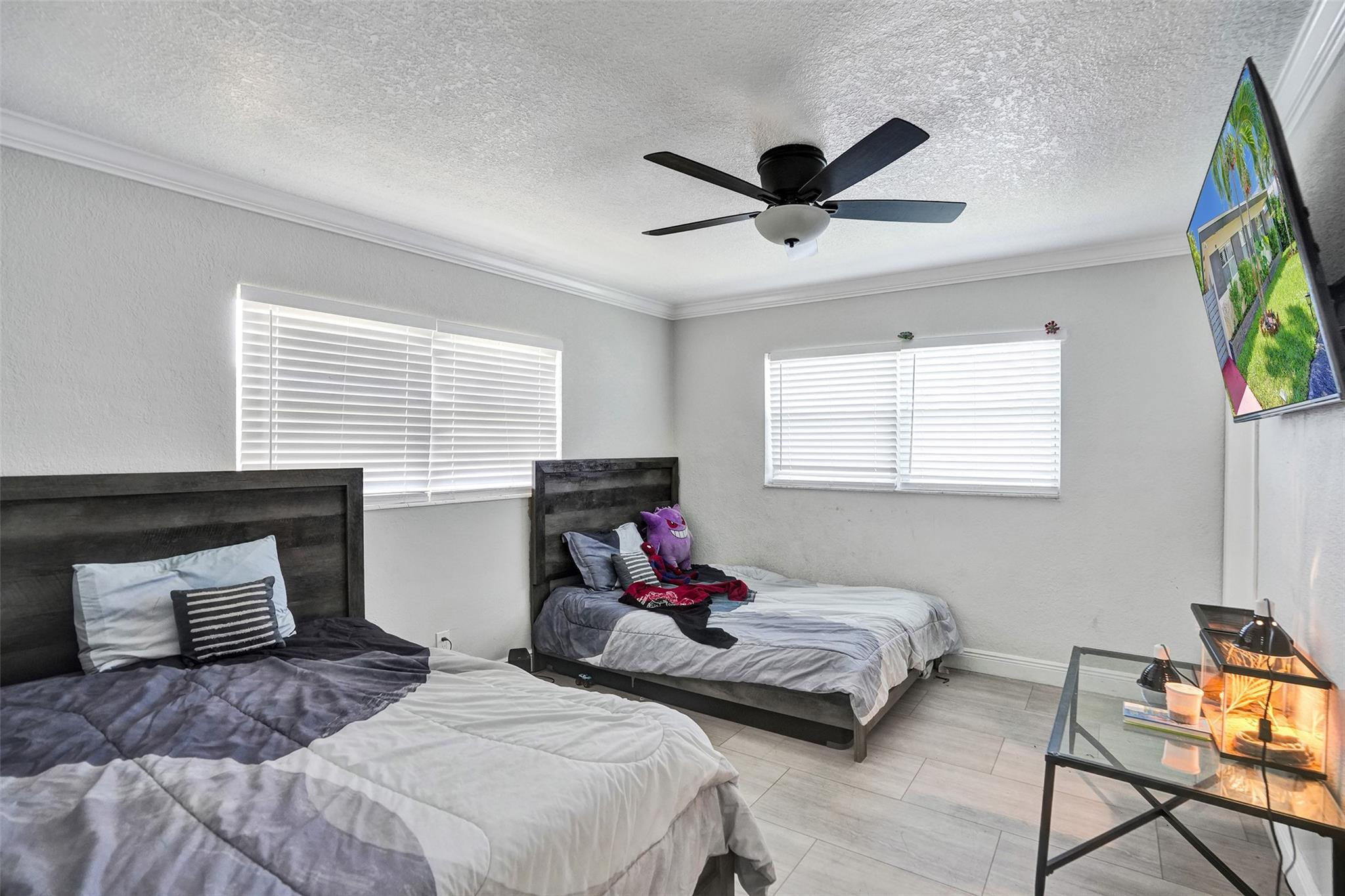 Bedroom with two beds, dark wood headboards, white blinds, and a ceiling fan.