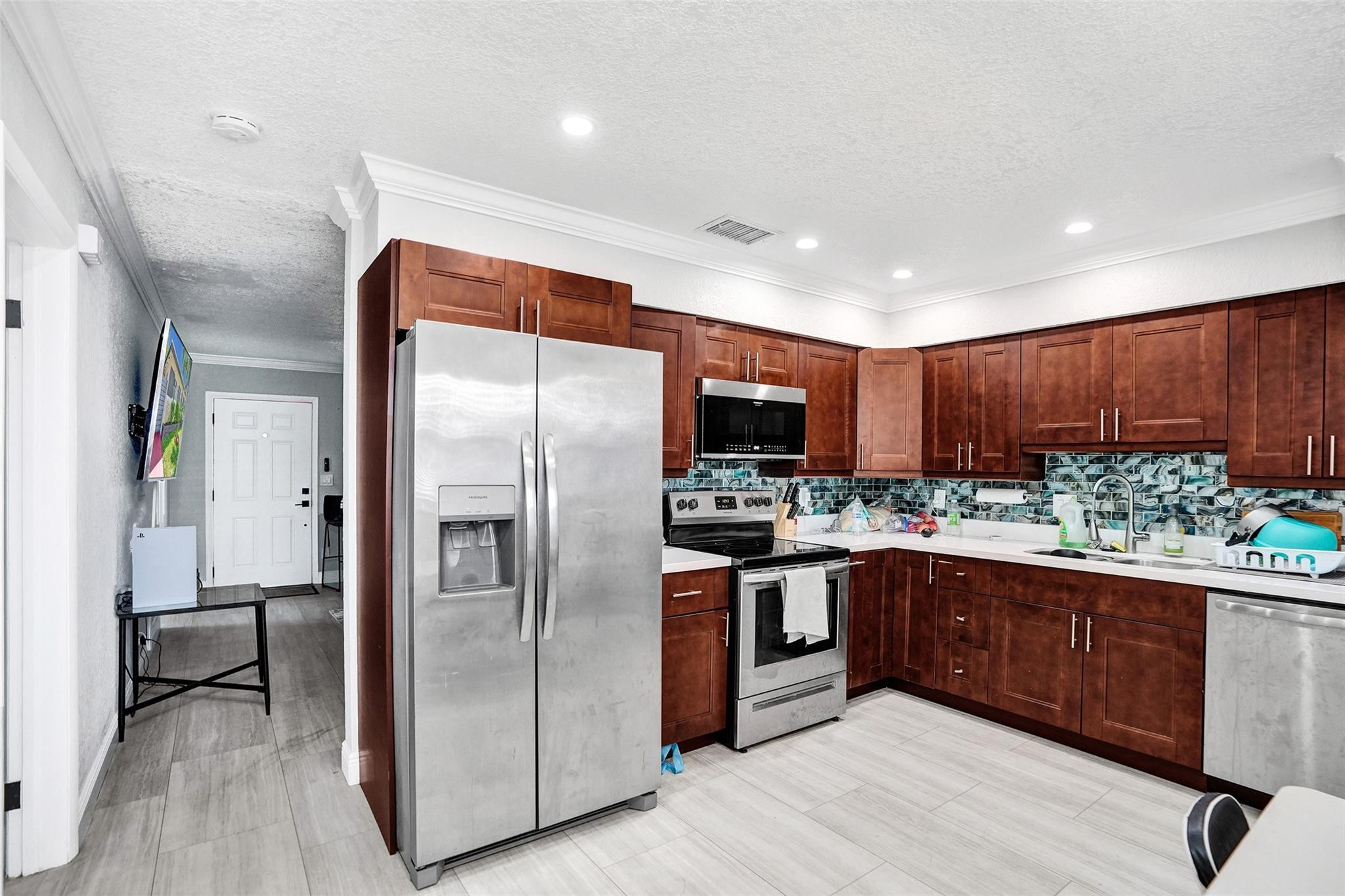 Kitchen with dark wood cabinets, stainless steel appliances, and a blue-gray mosaic backsplash.