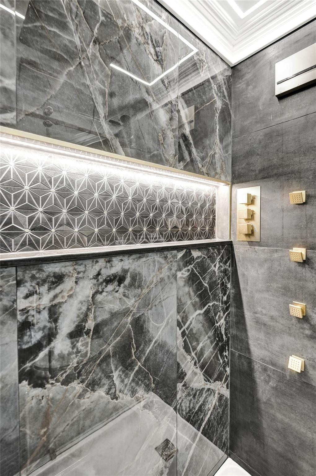 Modern shower with gray veined walls, a geometric tile accent, and gold-toned controls.
