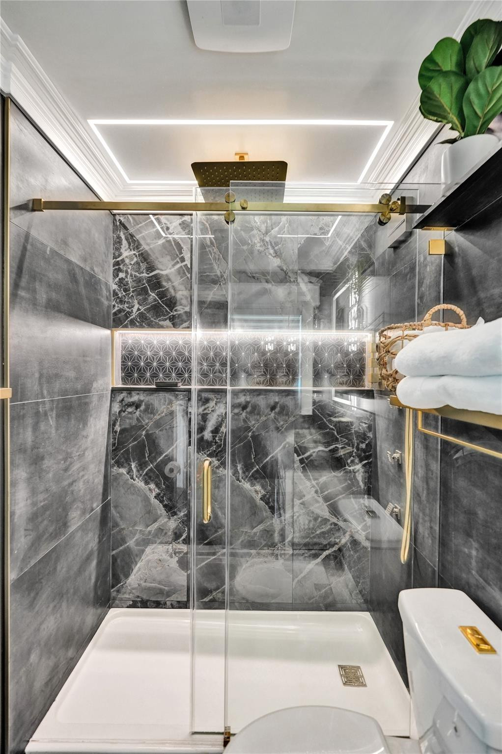 Bathroom shower with gray marble-look tile, glass enclosure, and gold hardware.