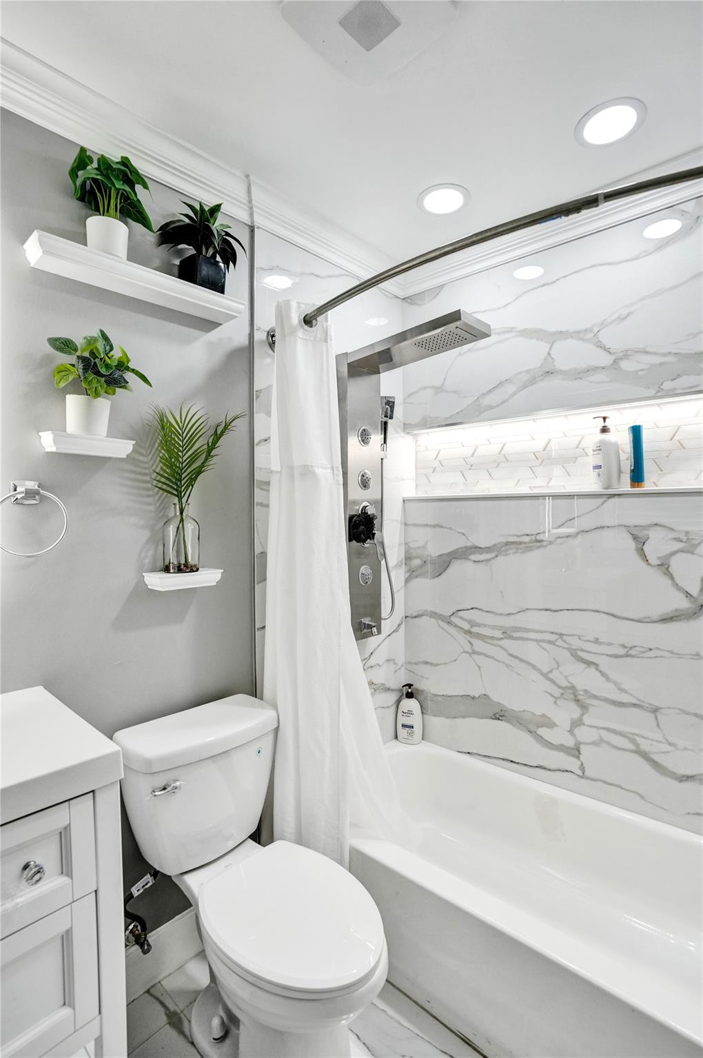 Bathroom with a marble-look tub and shower, white fixtures, and wall-mounted plant shelves.