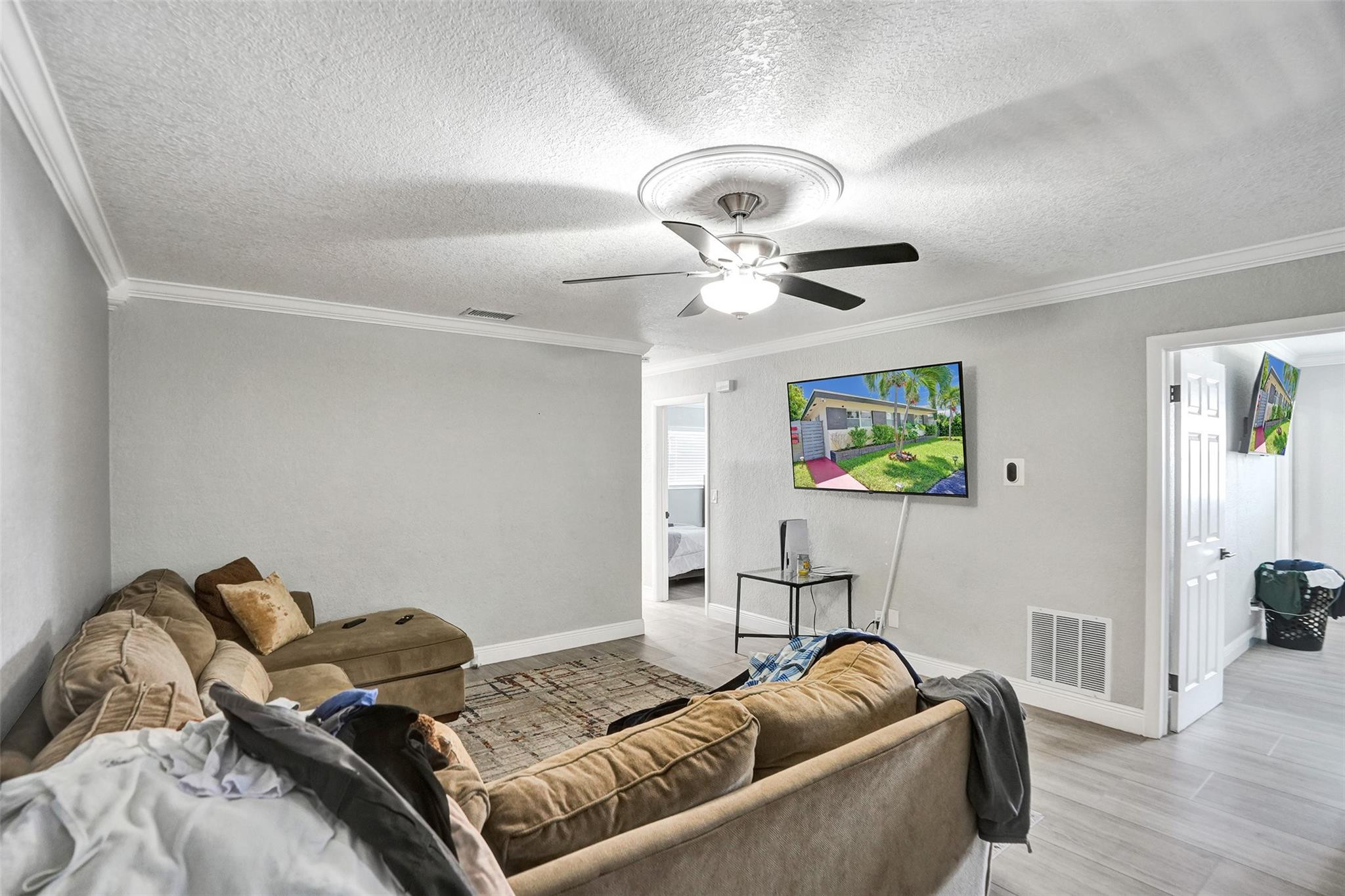 Living room with brown sectional sofas, a ceiling fan, and a television showing the home exterior.