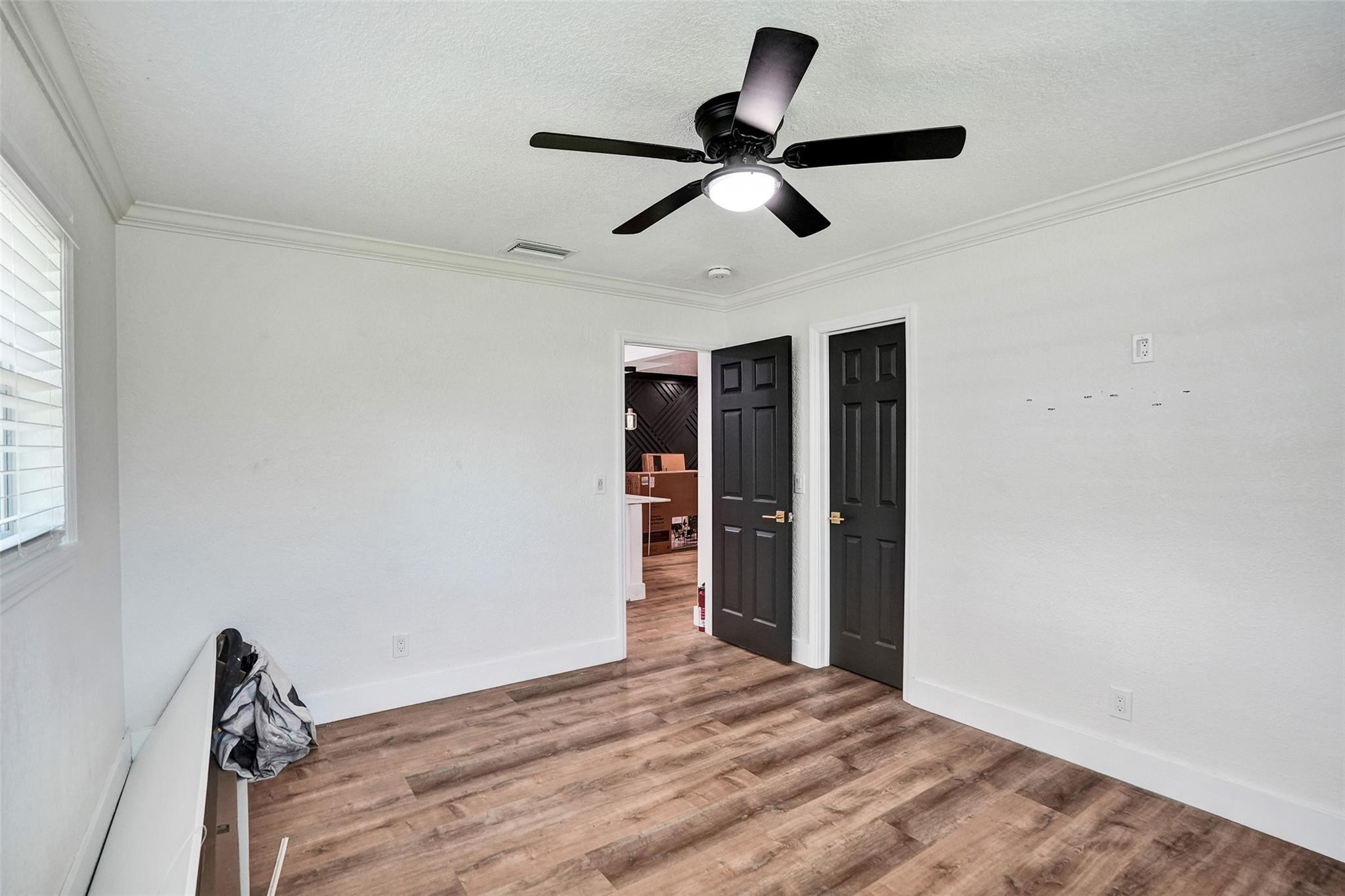 Empty bedroom with wood-look flooring, black ceiling fan, and two black doors.