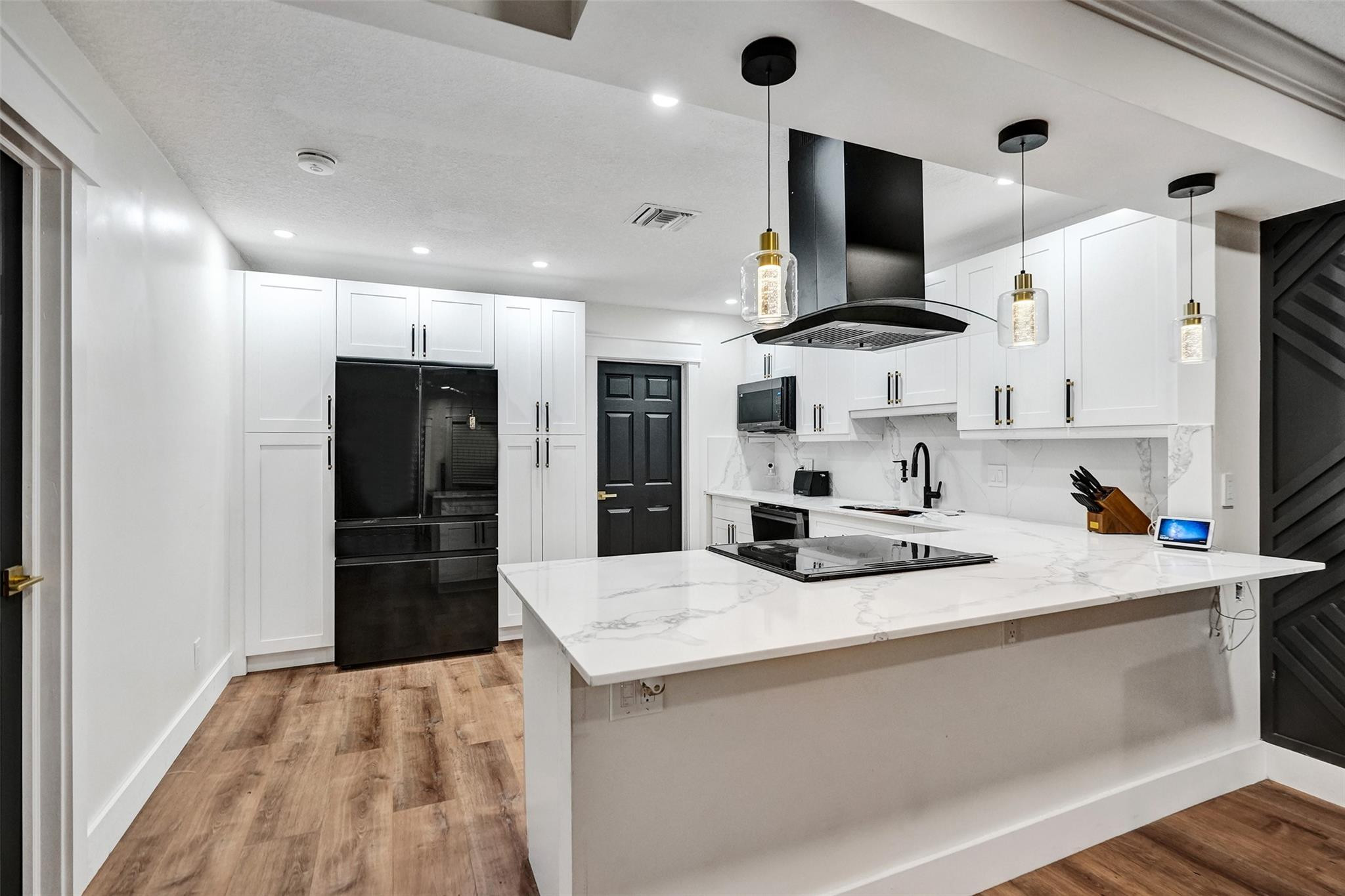 Modern white kitchen with a large veined quartz island, black appliances, and glass pendant lights.