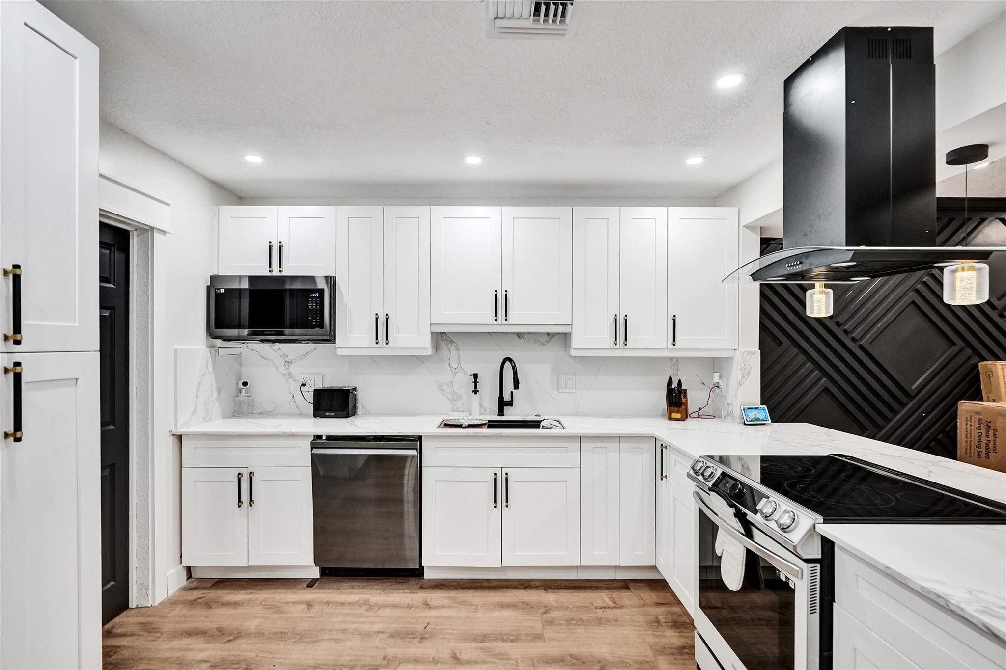 Renovated kitchen with white cabinets, stainless appliances, and a black geometric backsplash wall.