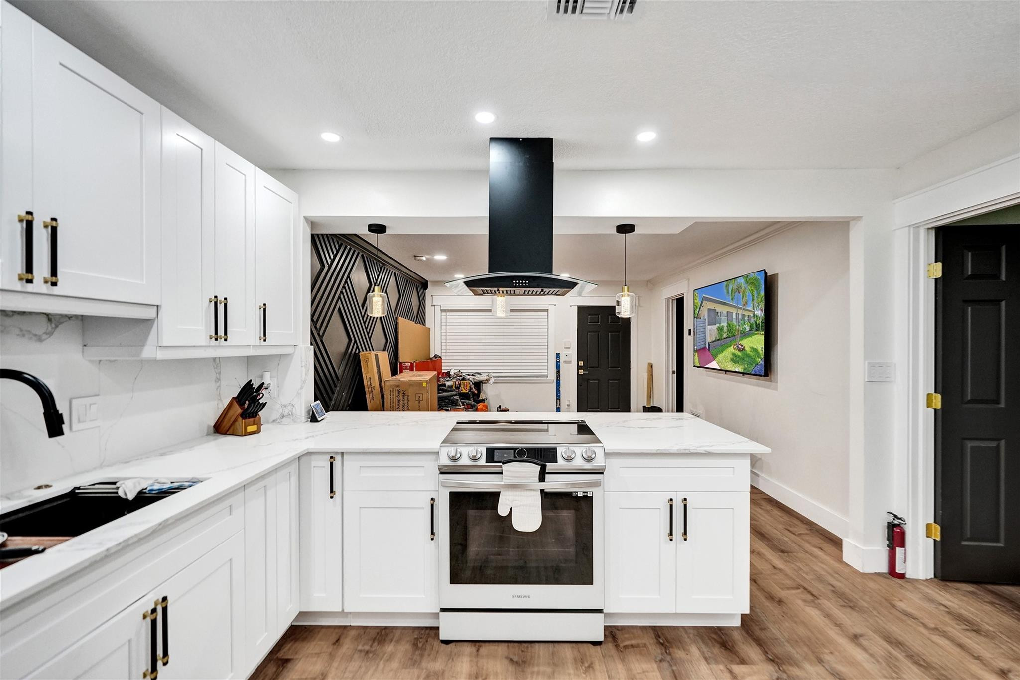 Modern white kitchen with marble-look counters, a stainless range, and a bold black geometric accent wall.