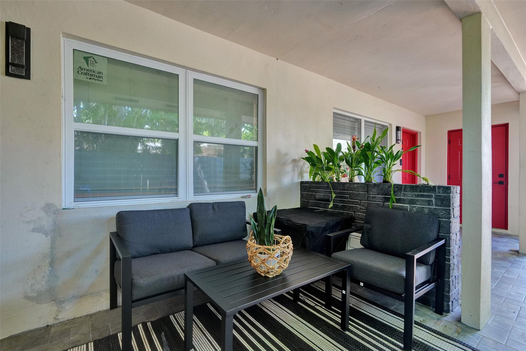 Covered patio with dark seating, potted plants, a striped rug, and bright red doors.